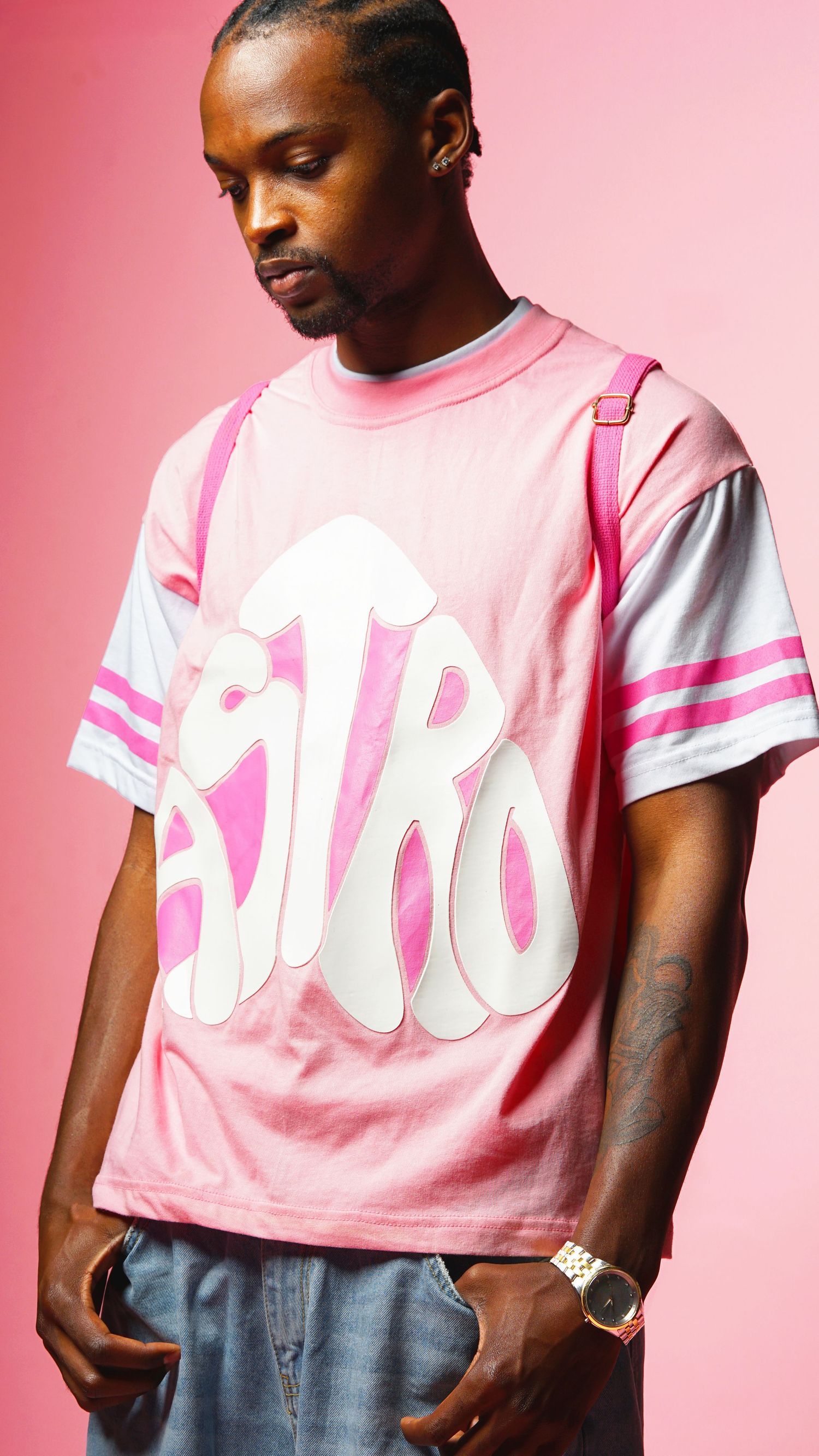 A fashion model wearing a pink and white streetwear t-shirt poses against a pink backdrop.