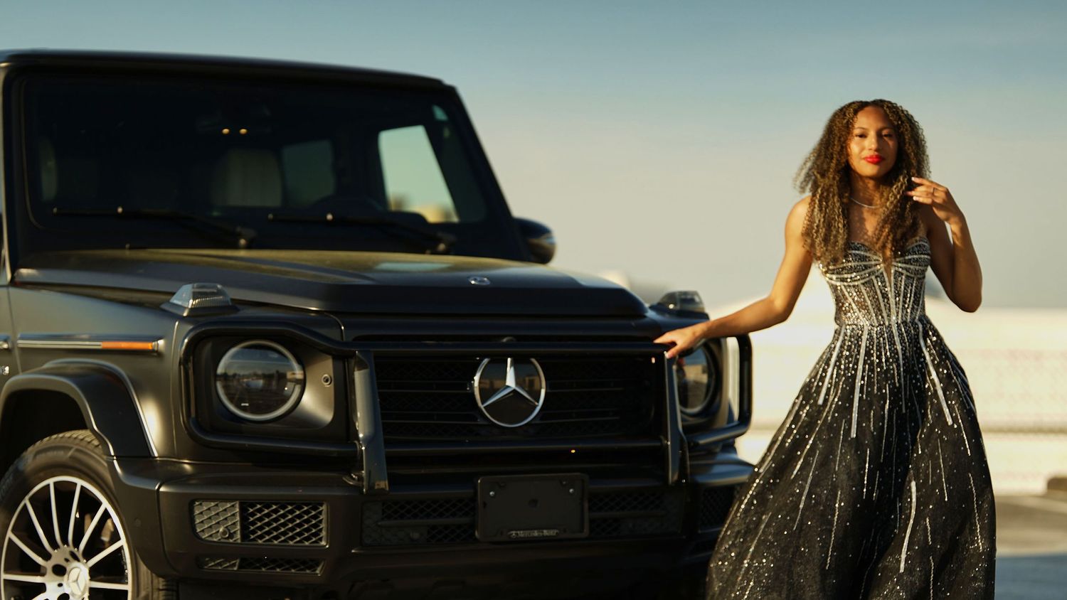 Glamorous photoshoot featuring black SUV and evening gowns in outdoor location.
