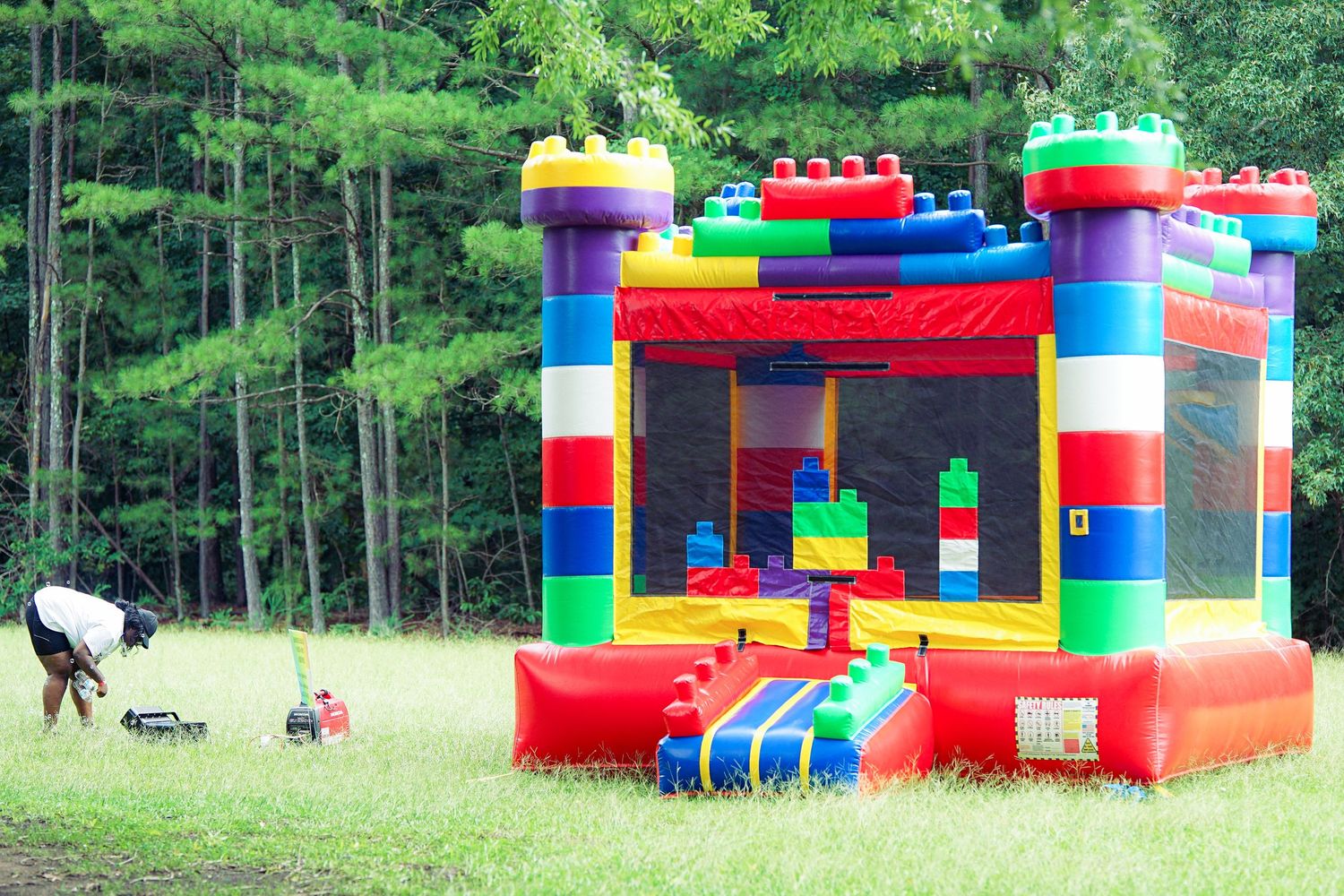 Colorful Lego-themed bounce house inflatable castle set up on grass at outdoor children's event.
