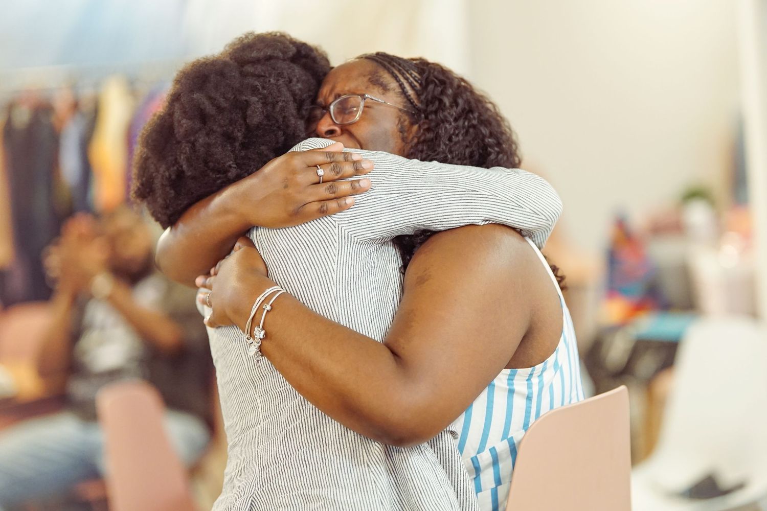 Two women sharing a warm embrace, smiling joyfully in a bright indoor setting.