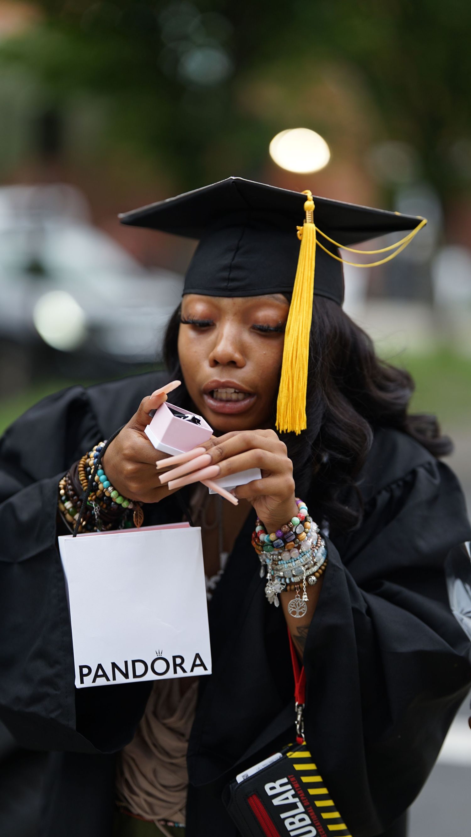 Graduate in academic regalia poses with Pandora sign during outdoor photo session.