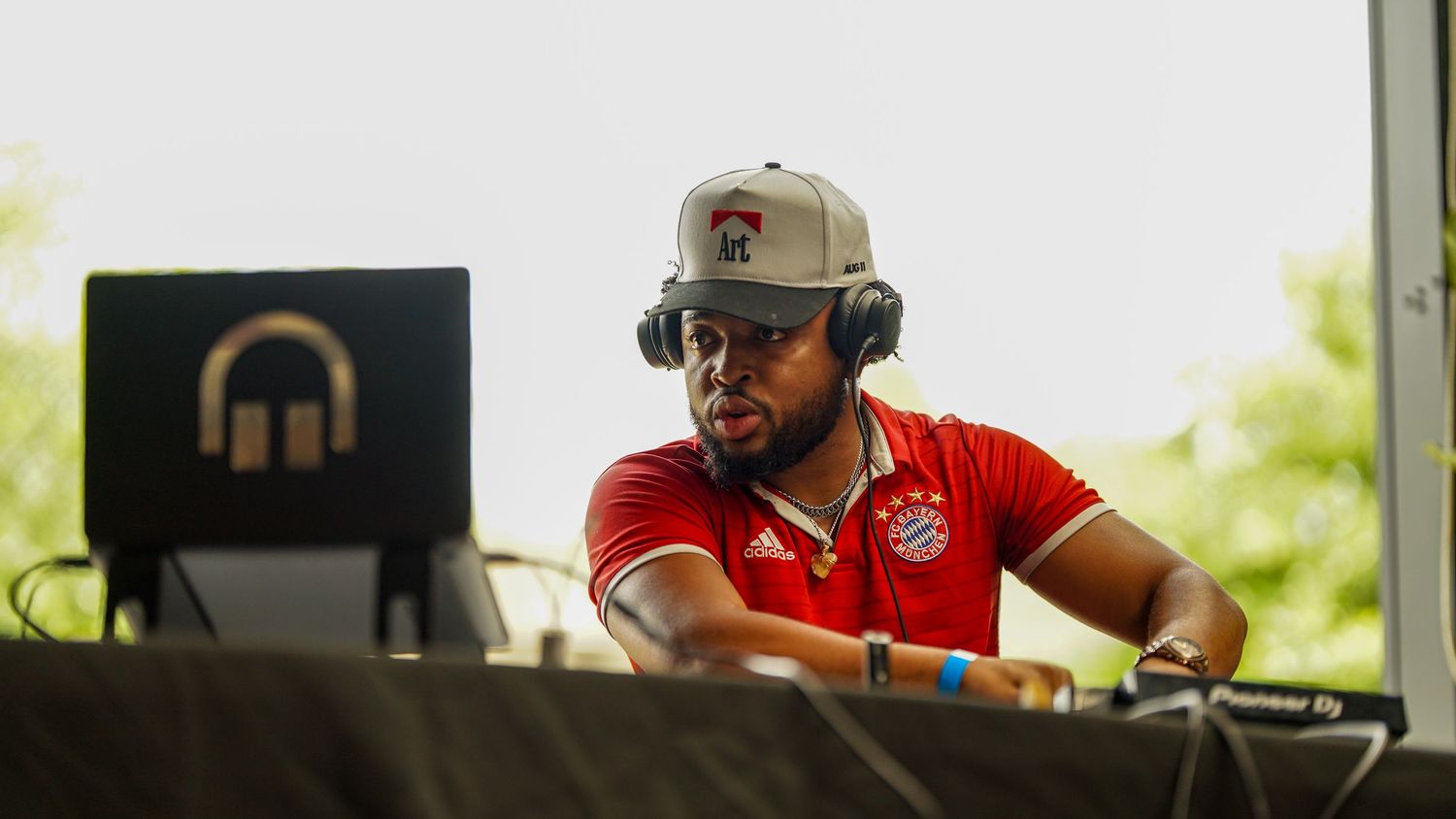 DJ wearing headphones and red shirt performs at an outdoor event.