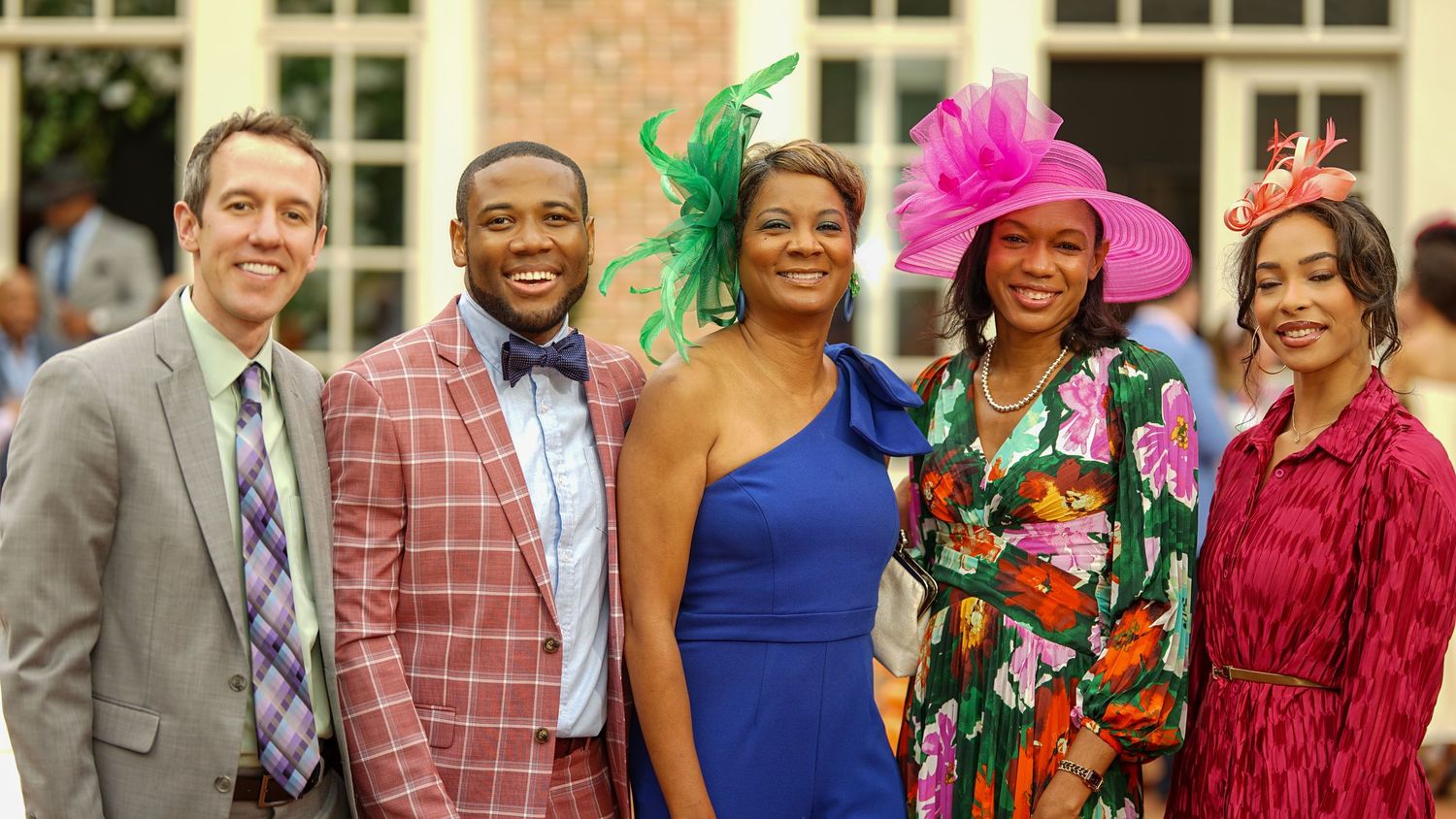 Group photo of people in formal attire with colorful accessories at a brick building.
