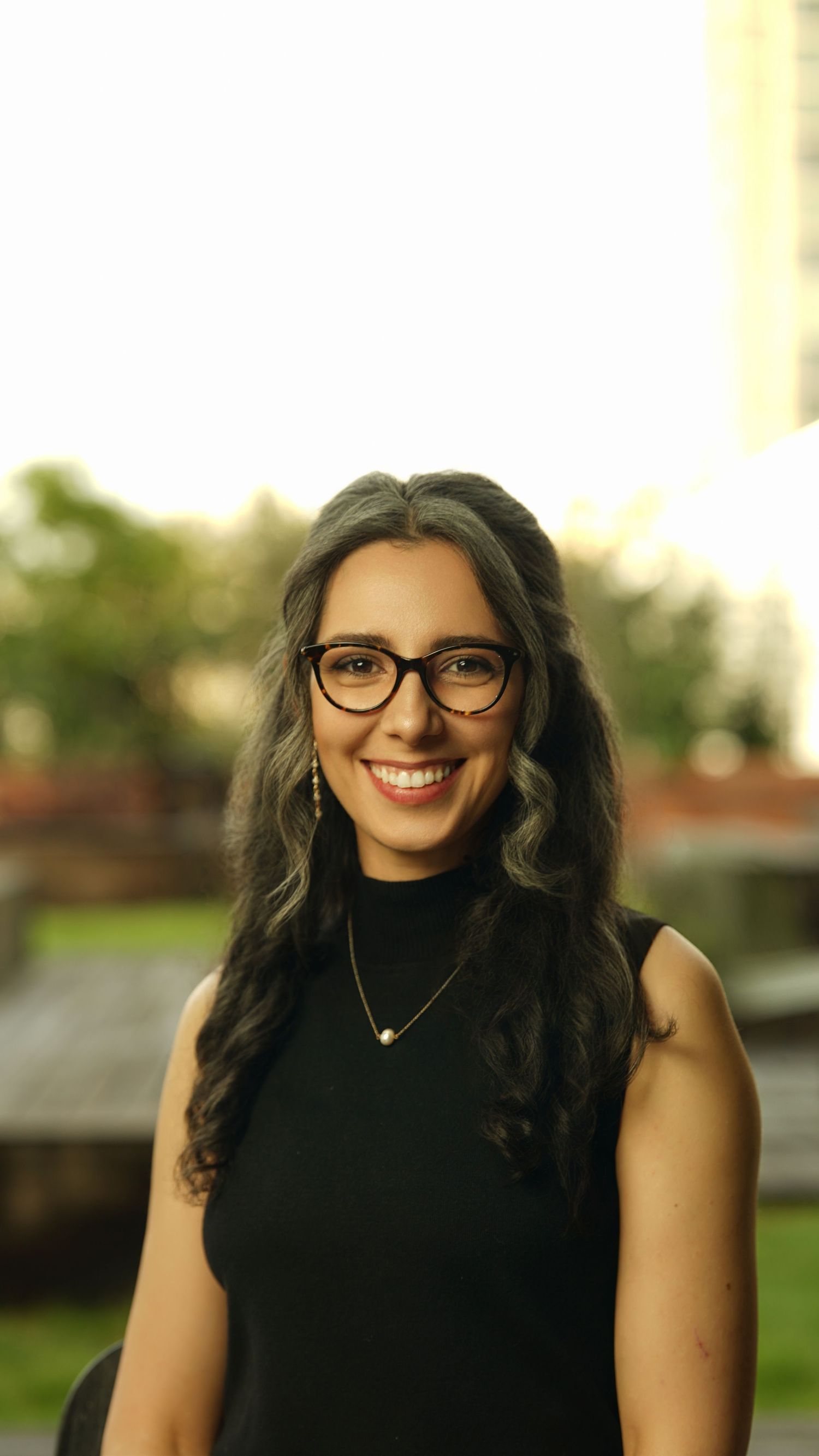 Portrait of person in black sleeveless top wearing glasses and necklace with a warm smile.