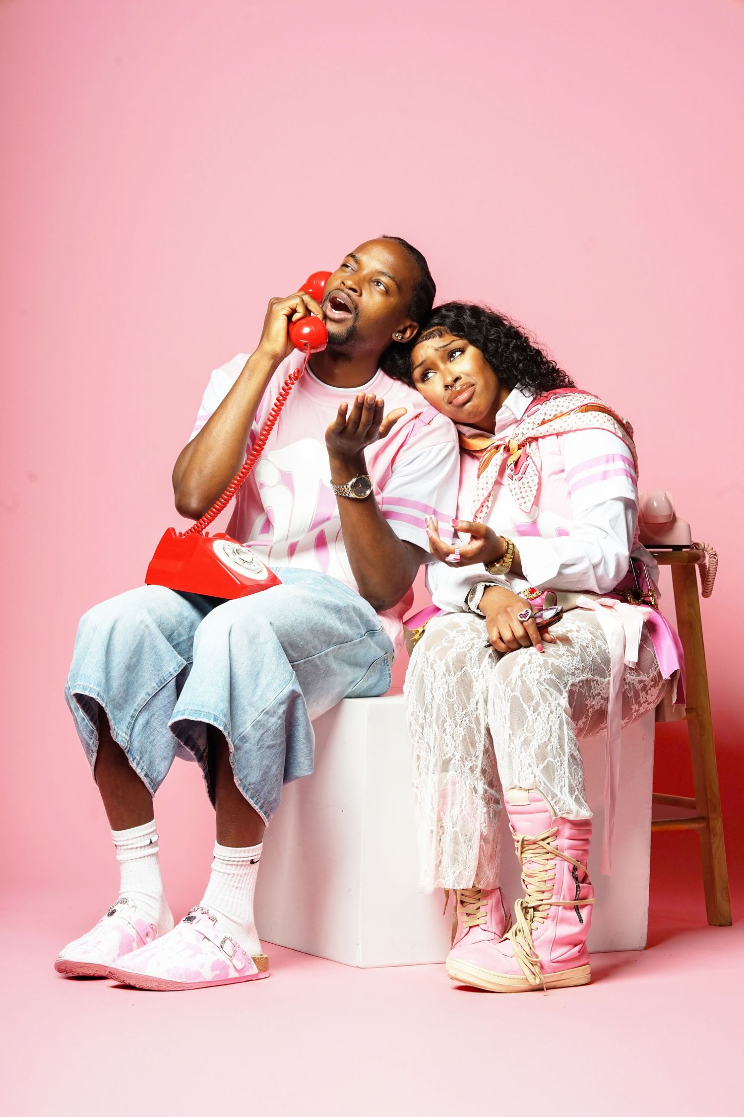 Casual fashion shoot with models lounging on white blocks against pink background.