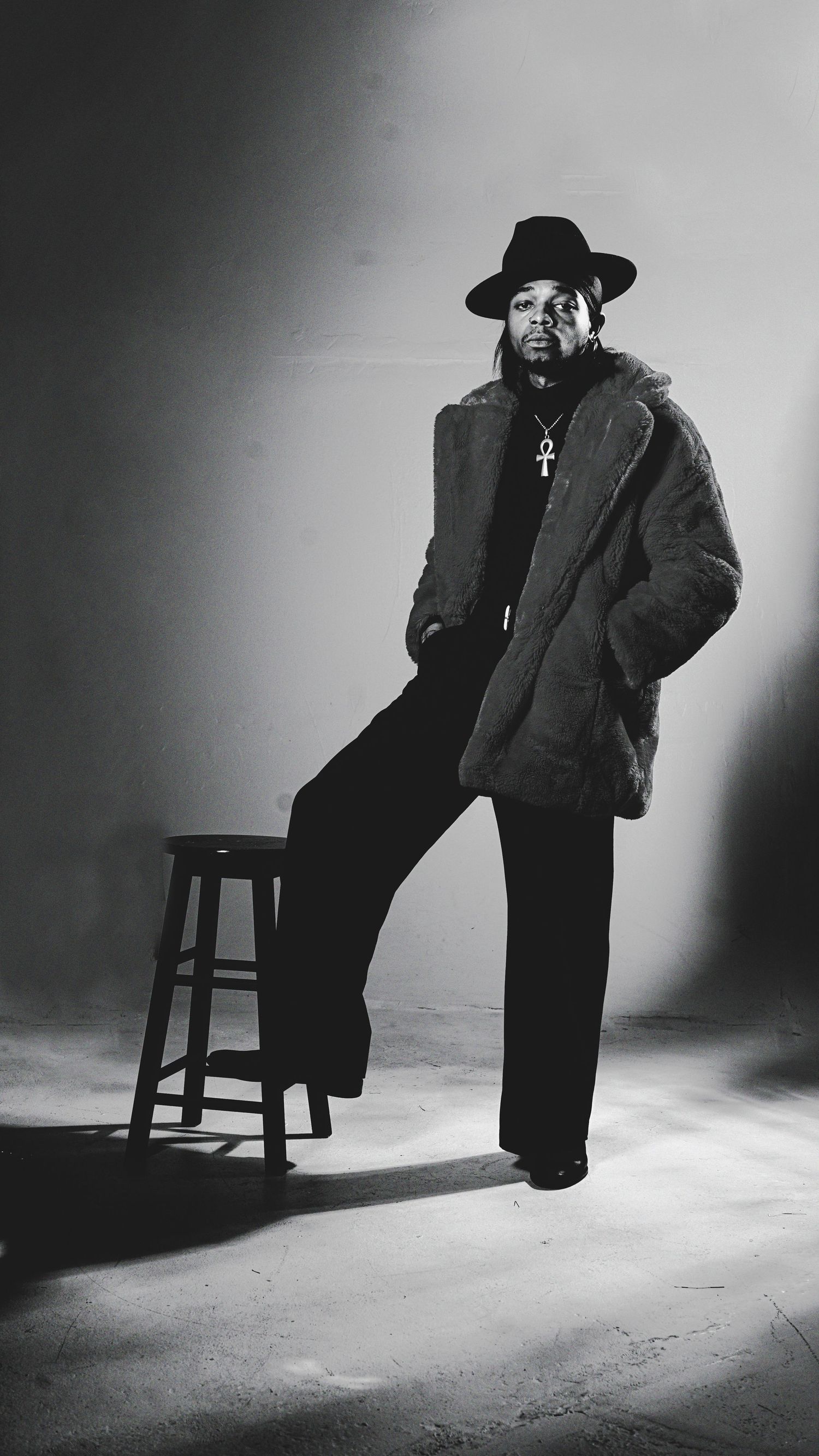 Film noir style black and white photos of a figure in a hat and coat posing with a stool.