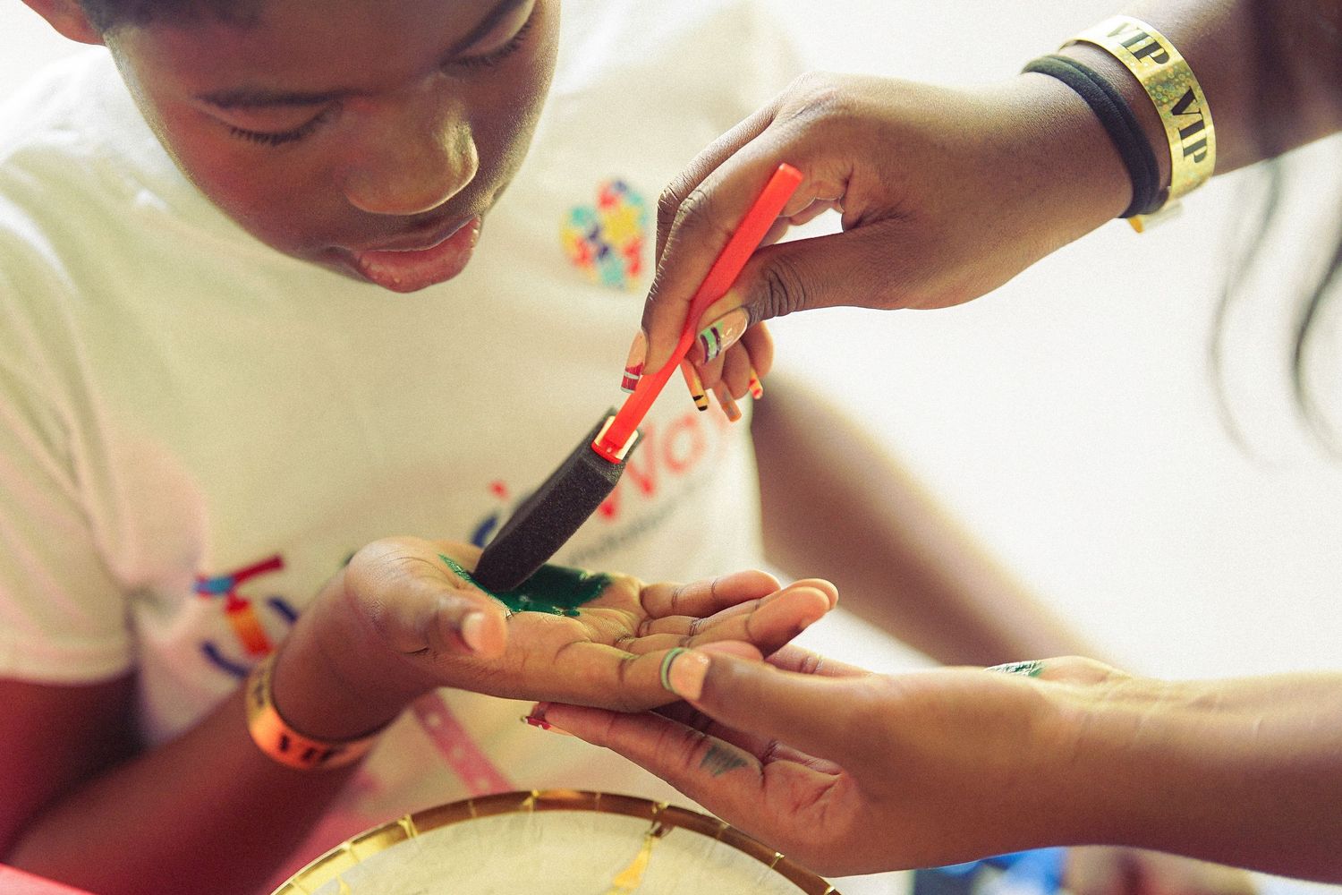 Artist applying intricate henna design on a young girl's hand using a red applicator pen.