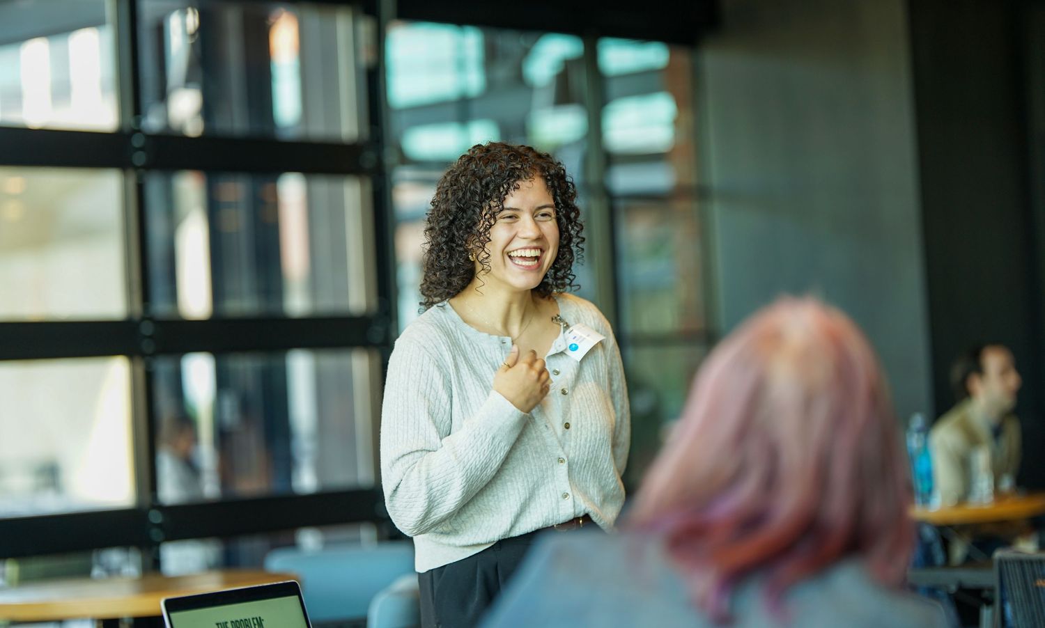 Smiling woman with curly hair presenting confidently in a modern office meeting room.