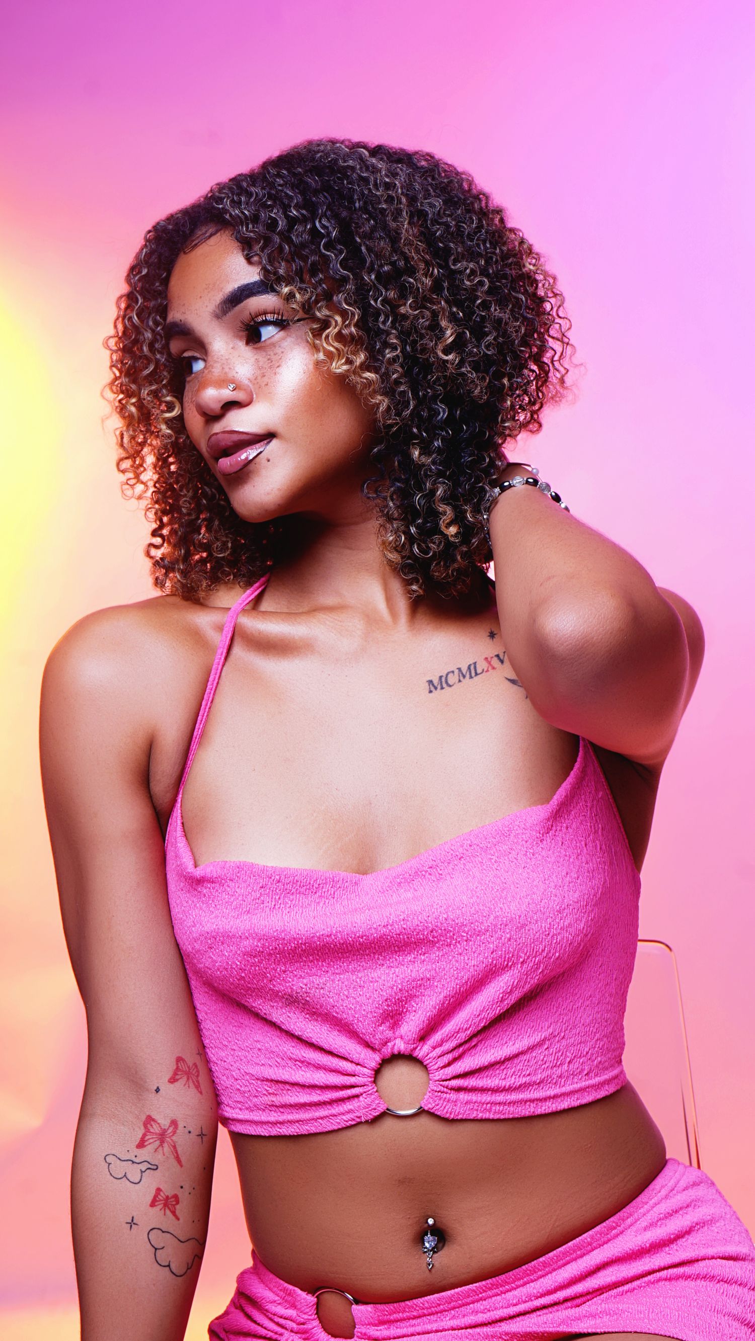 Fashion portraits in pink lighting wearing a sparkly pink crop top and natural curly hair.