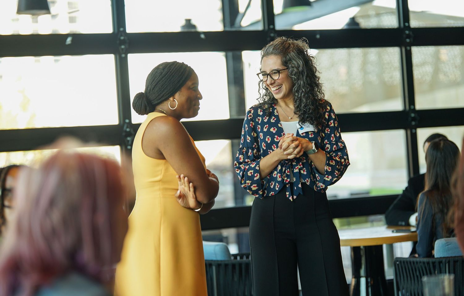 Two businesswomen smiling and networking at a professional corporate event indoors.