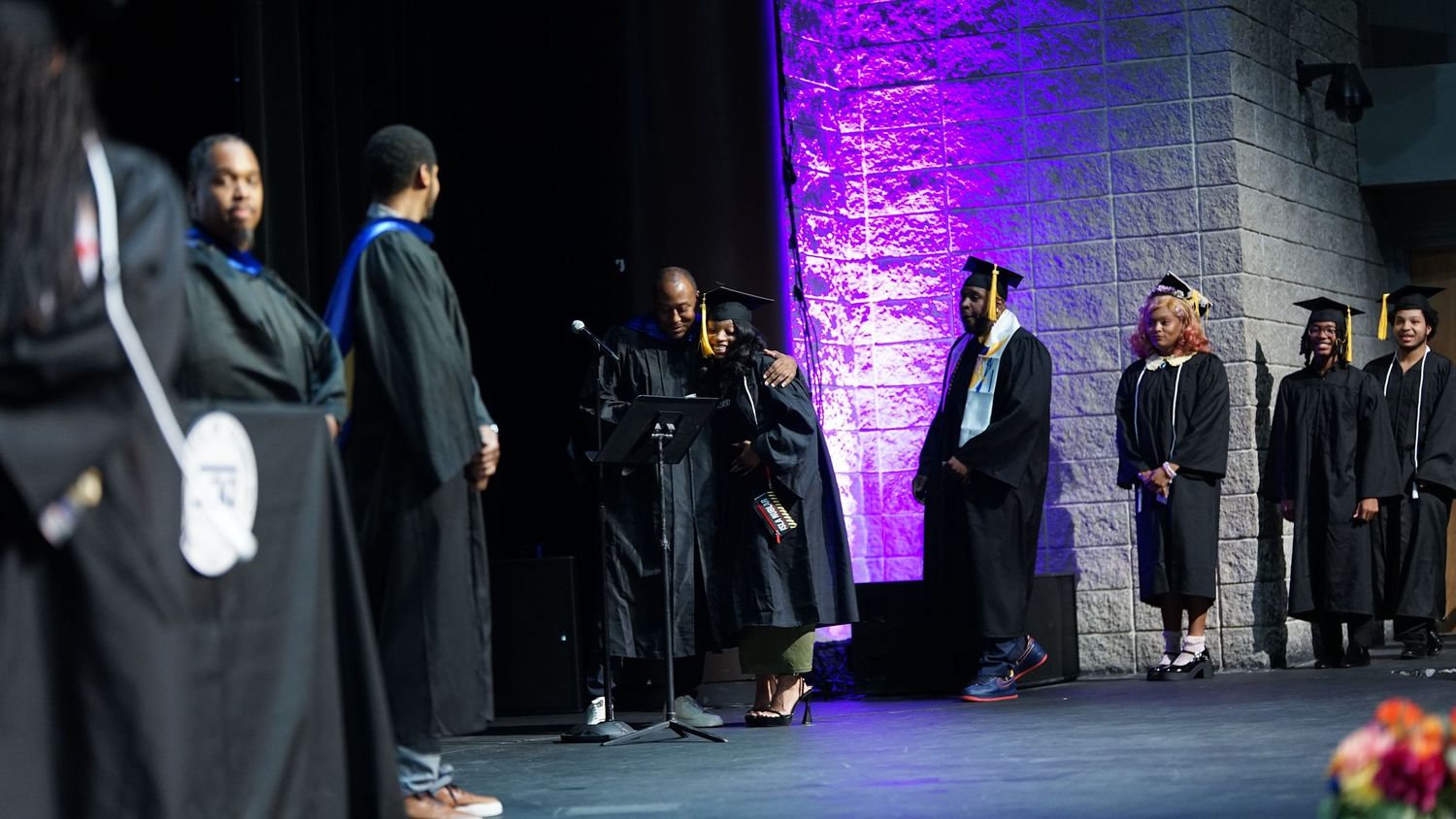 Graduation ceremony in dark venue with purple lighting illuminating stone walls.