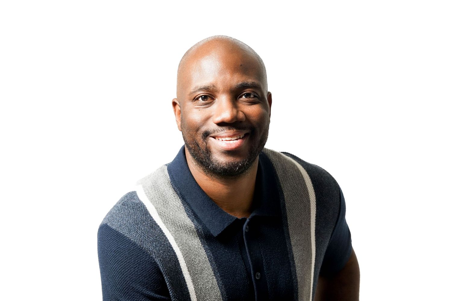 Smiling bald Black man wearing a navy striped polo shirt, posing against a white background.