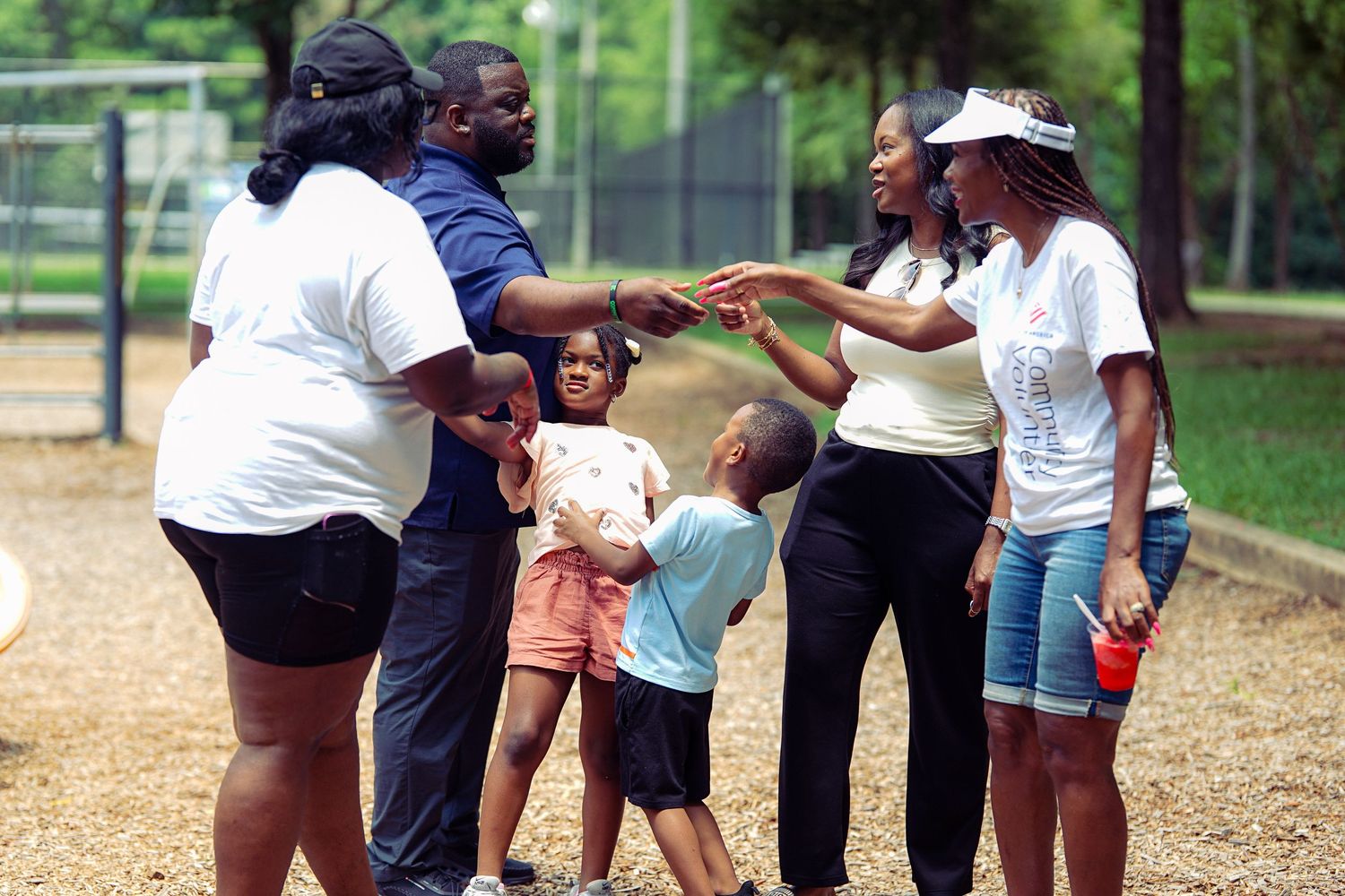 Families with children gather and interact outdoors at a park playground on a sunny day.