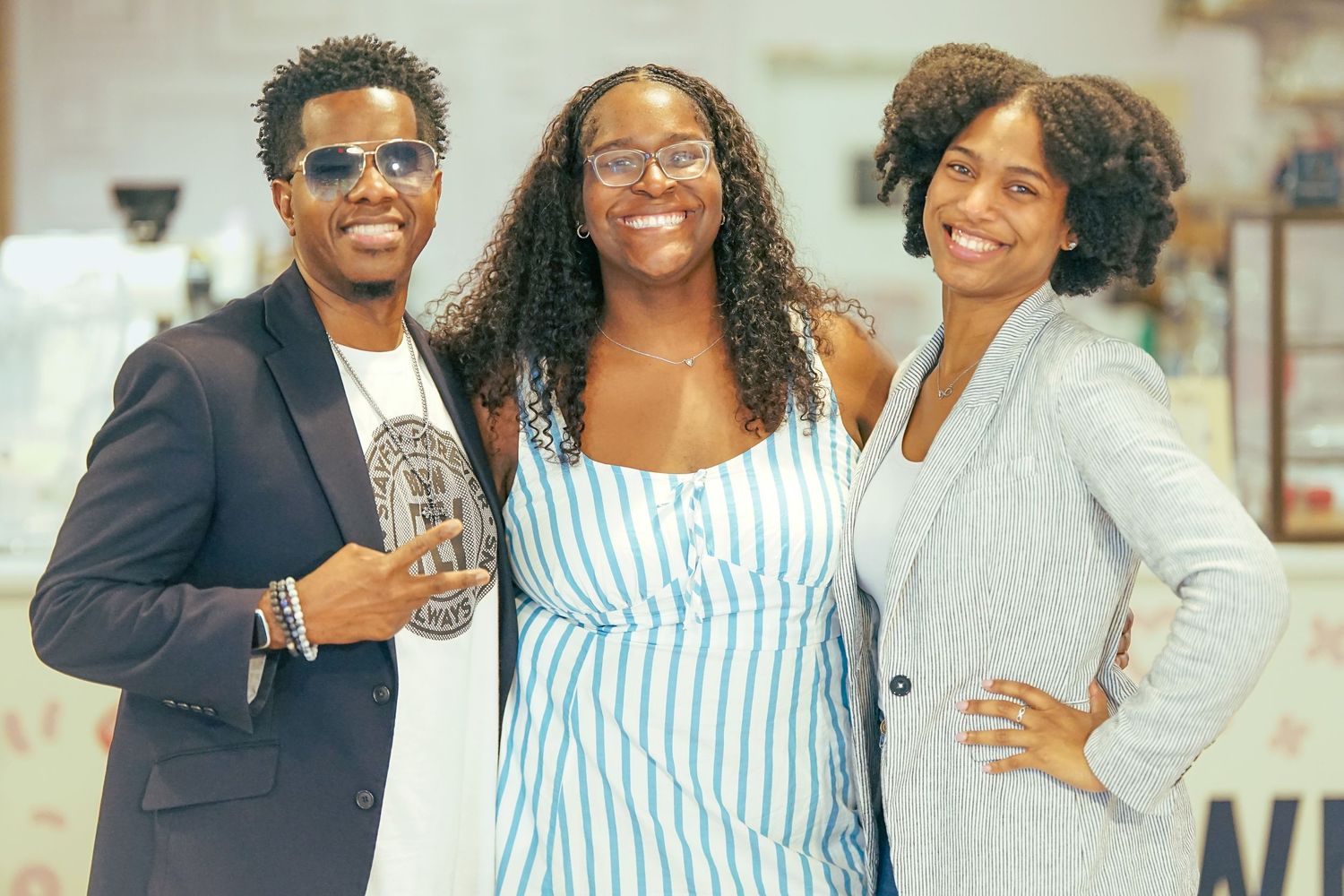 Three young adults smile and pose together for a photo at an indoor social event.