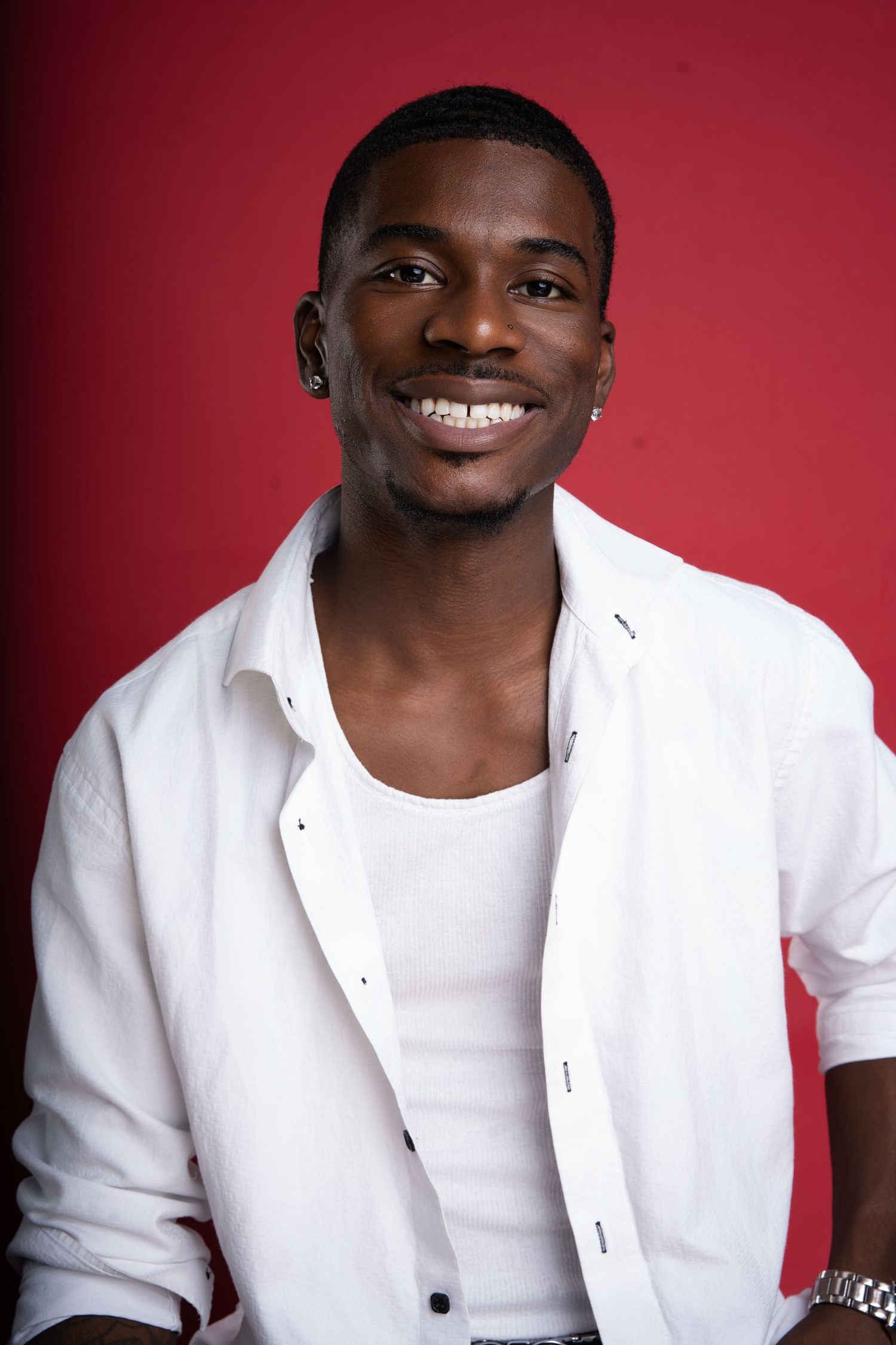 Portrait of person in white button-down shirt smiling against red background.