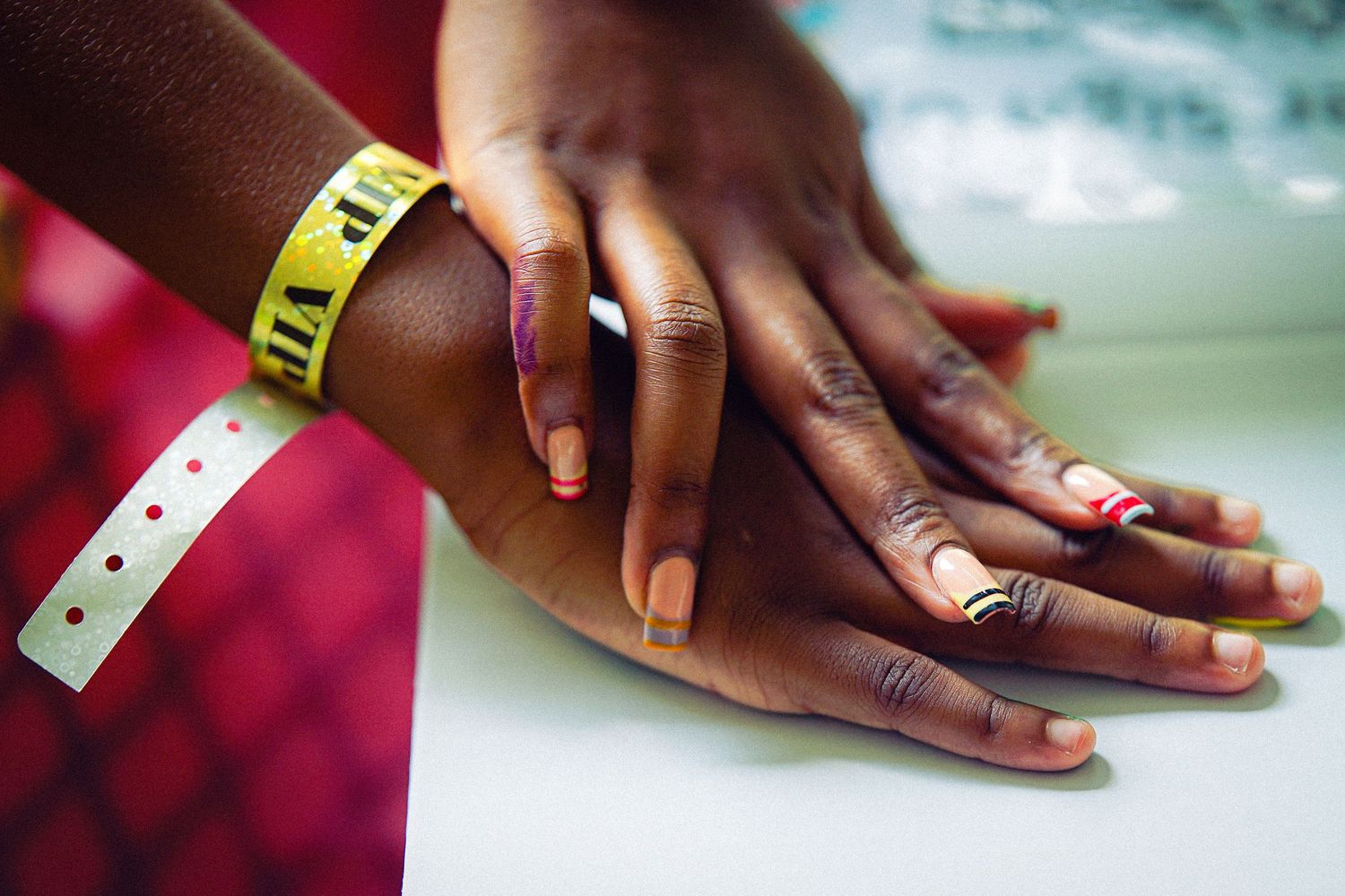 Close-up of hands with colorful nail polish and a yellow event wristband stacked together.