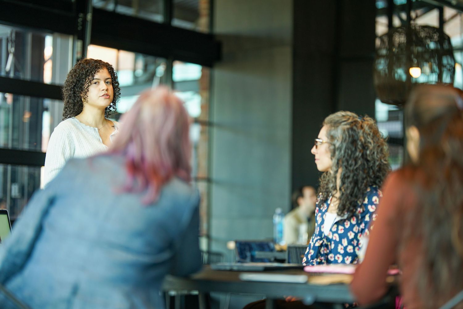 Woman presenting to a group of colleagues in a modern office meeting room during a business discussion.