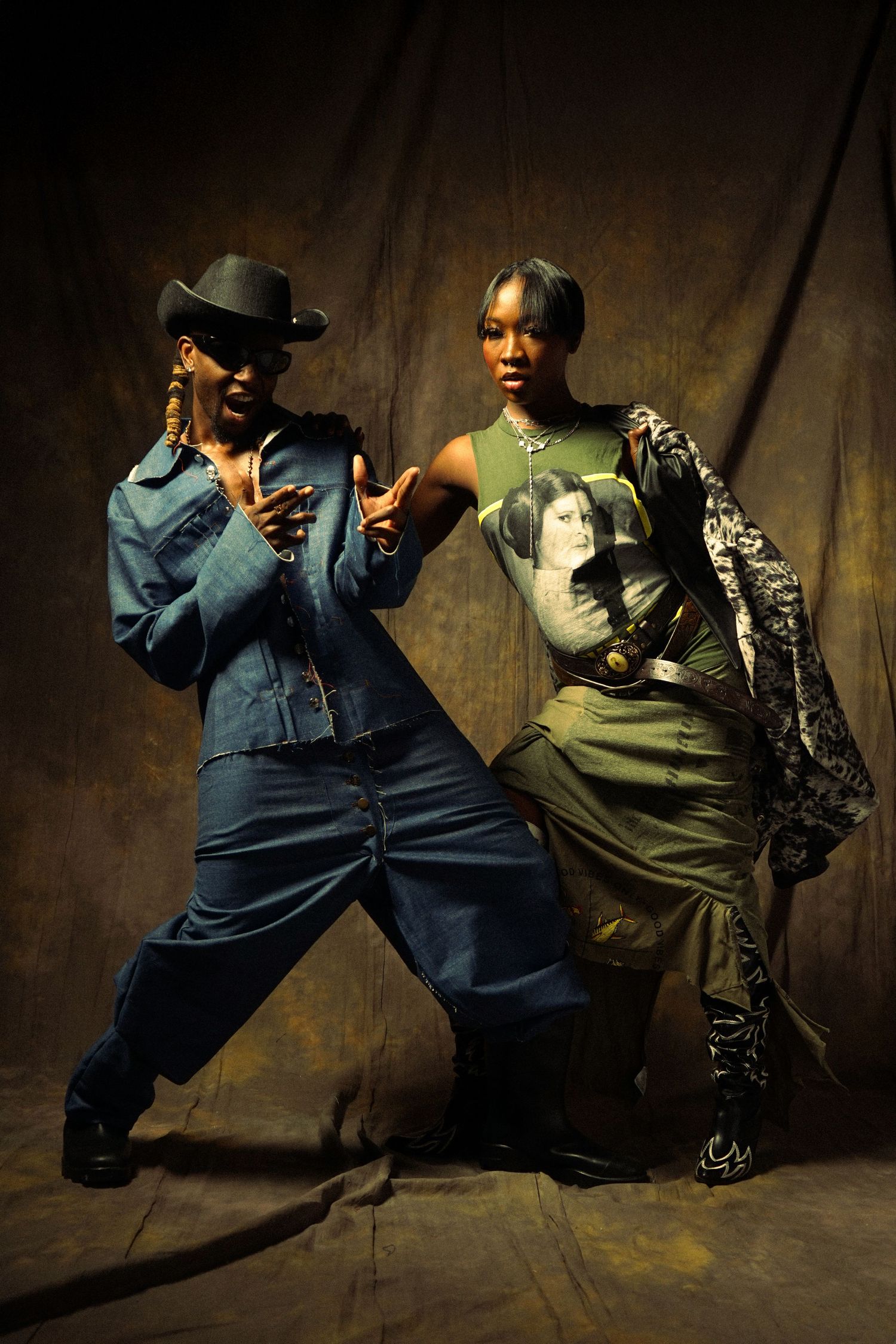 Two dancers perform a dramatic dance sequence in casual clothing against a dark rustic backdrop.