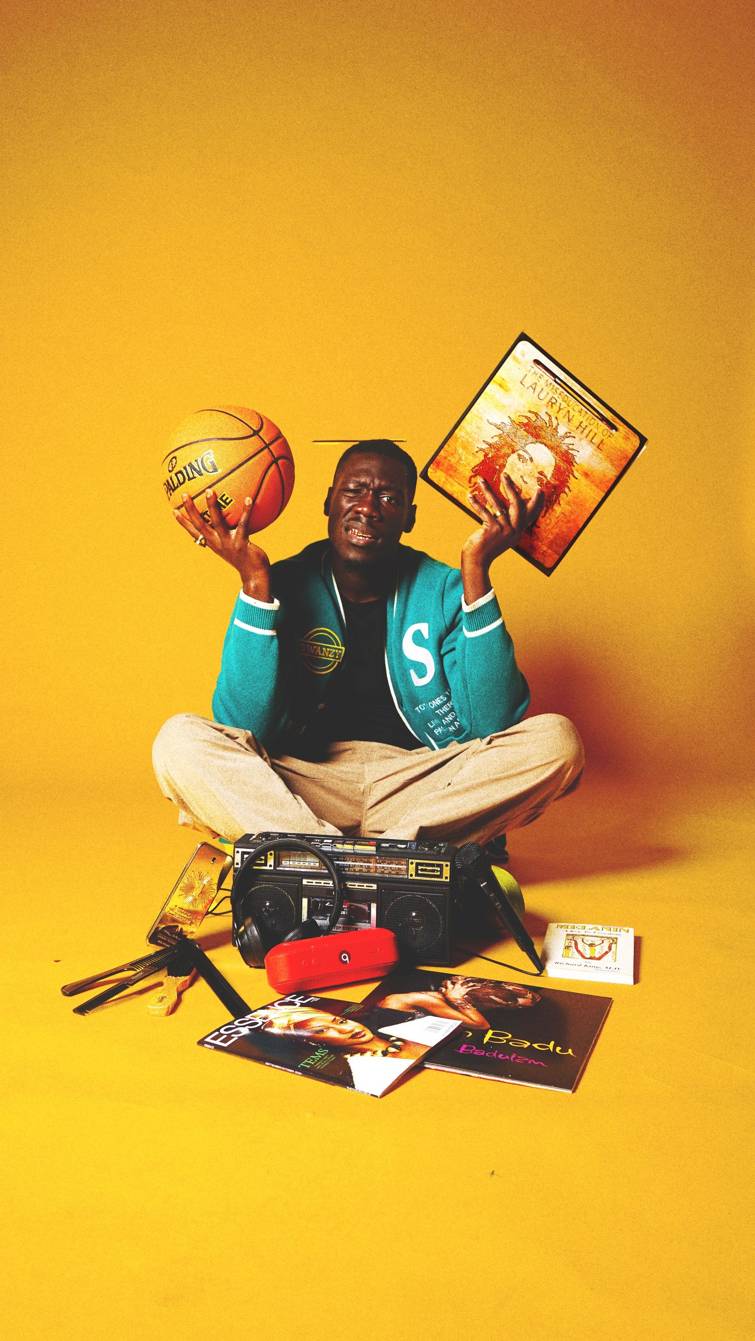 Person in turquoise shirt sitting cross-legged with books and media scattered around on orange background.