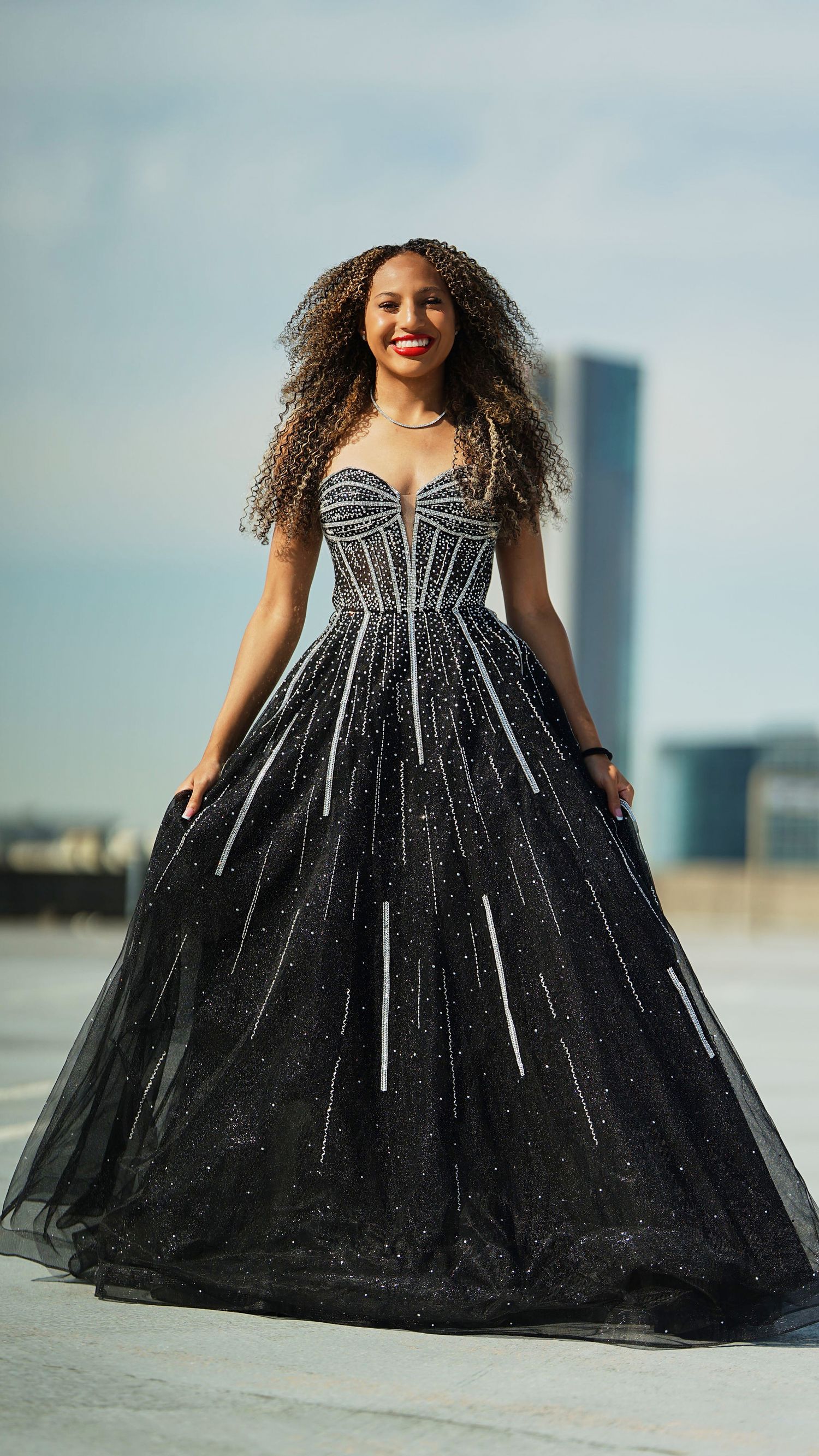 Dramatic black tulle gown with sparkly details photographed against sky backdrop.