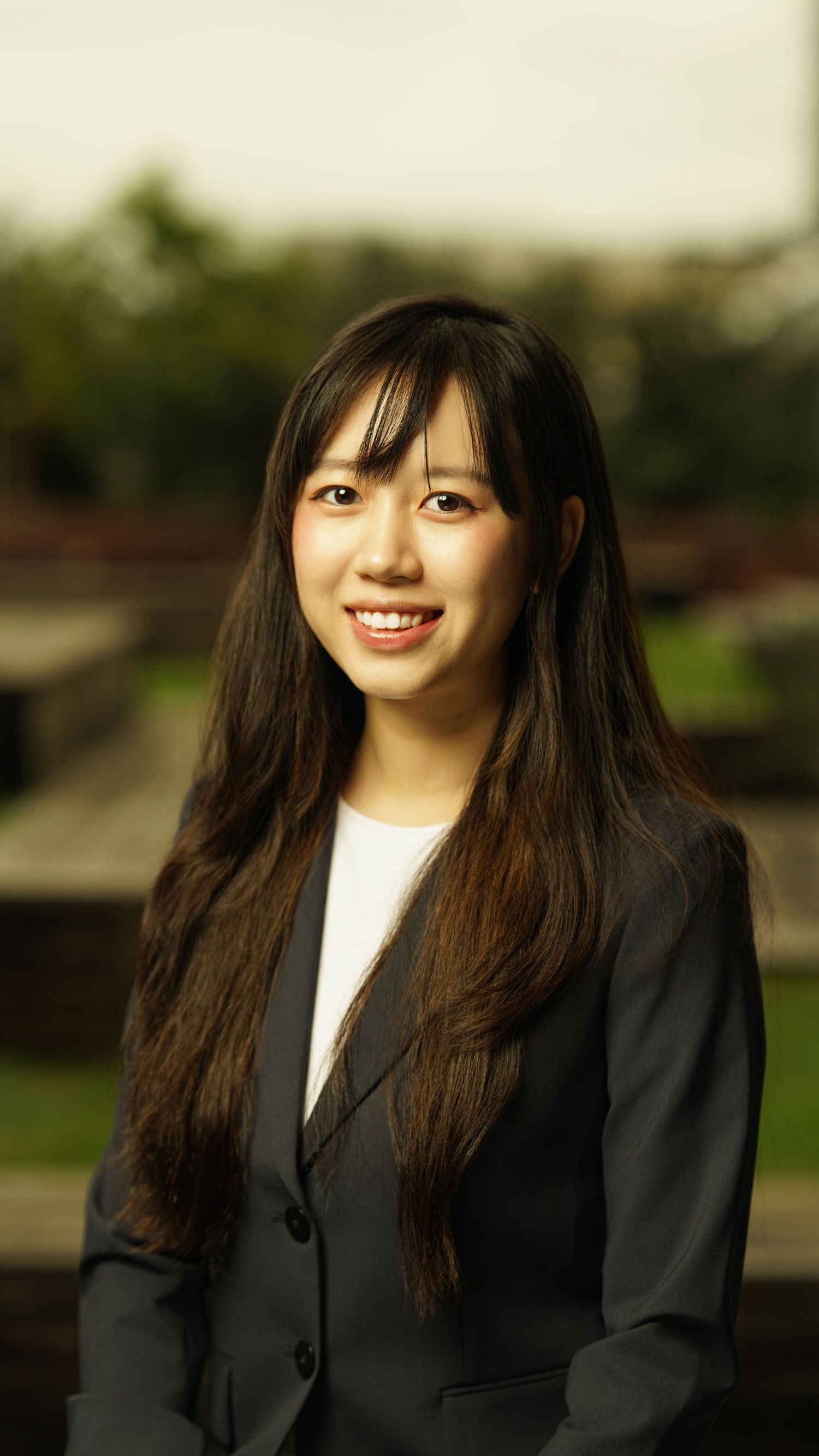 Professional in dark blazer and white top smiles during outdoor portrait session.