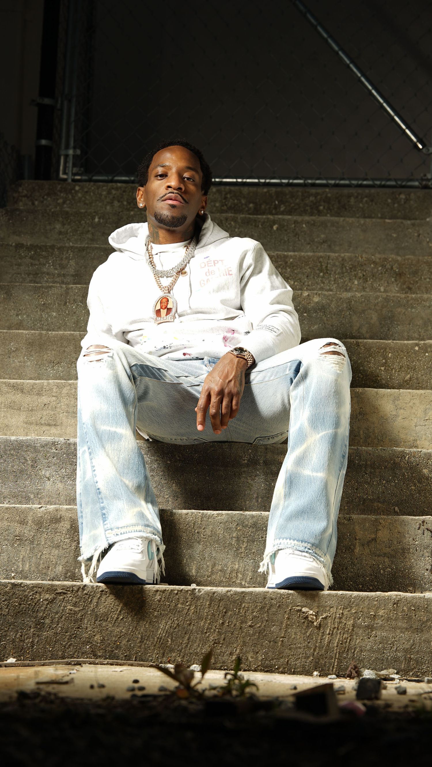 Person in white clothing sits casually on concrete steps in a dimly lit setting.