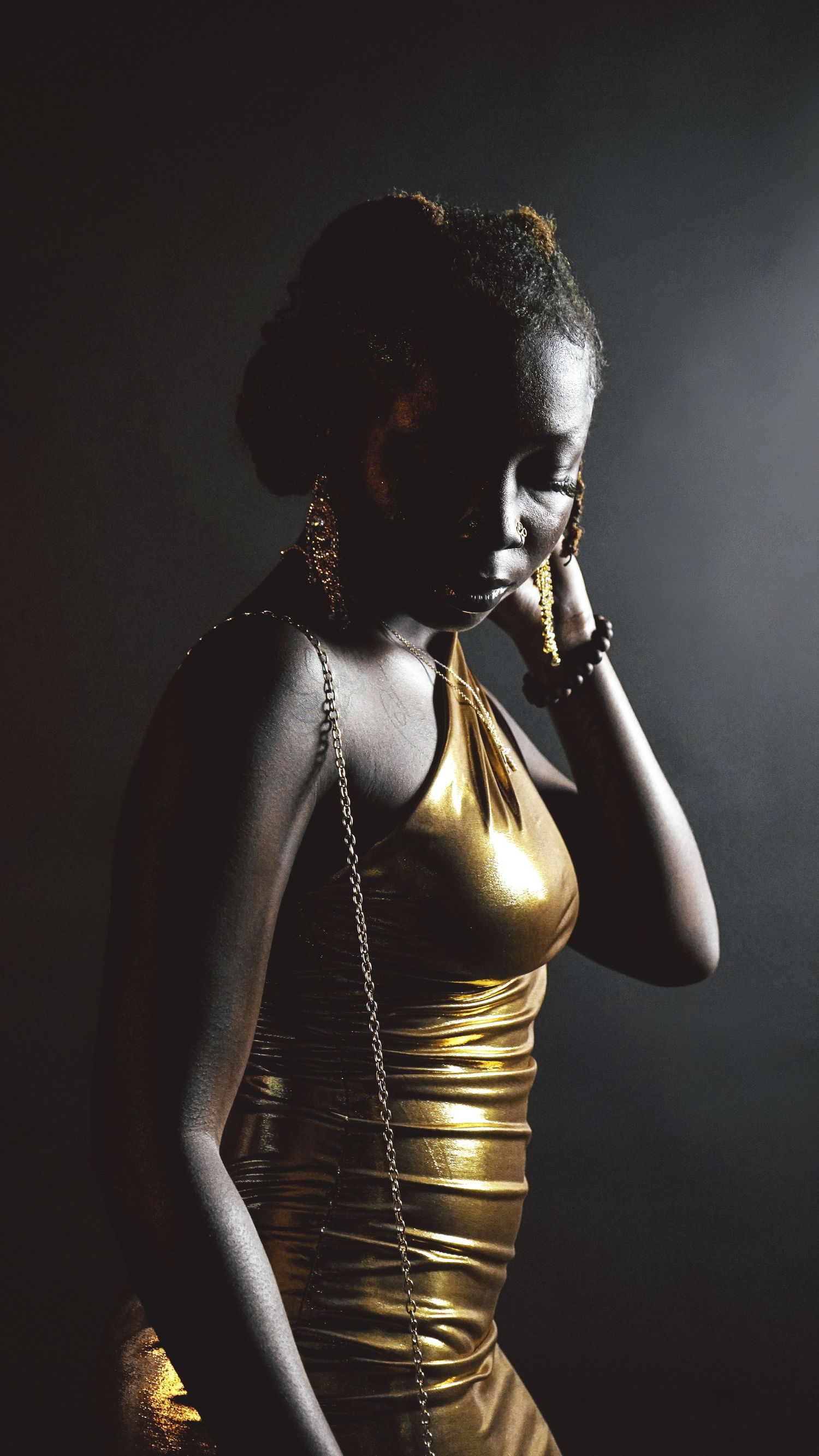Artistic portraits in dramatic lighting wearing a metallic gold top against dark background.