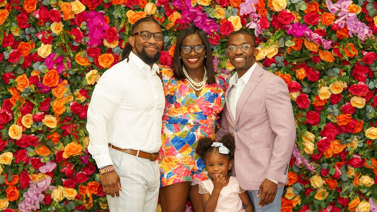 Group photo against colorful floral backdrop at formal event.