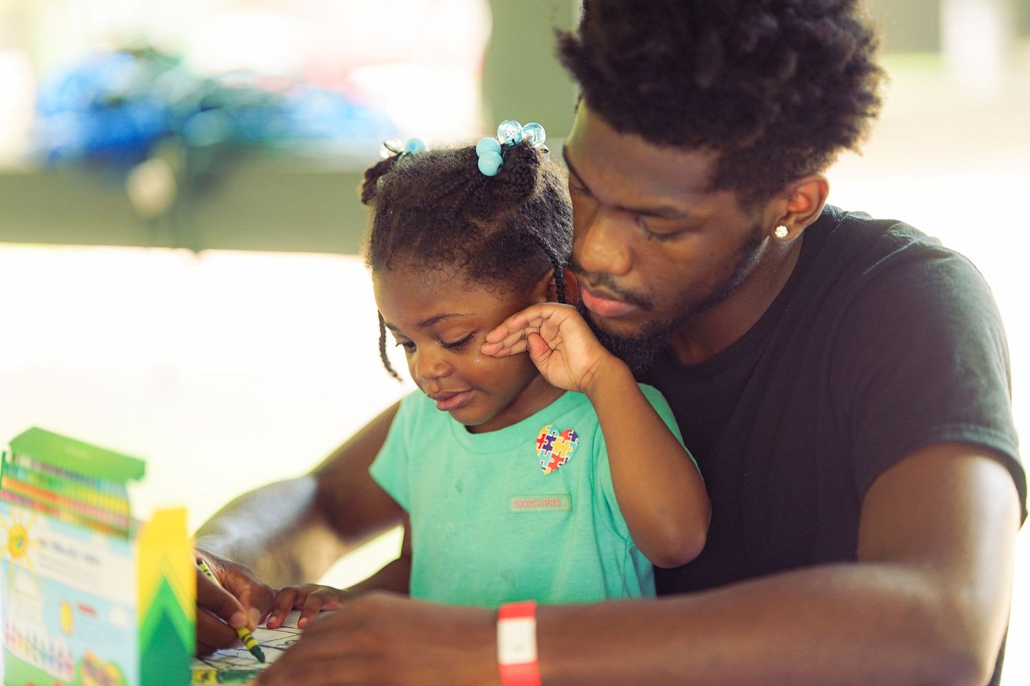 A young man tenderly holds a small girl as they look at a book together at an outdoor event.