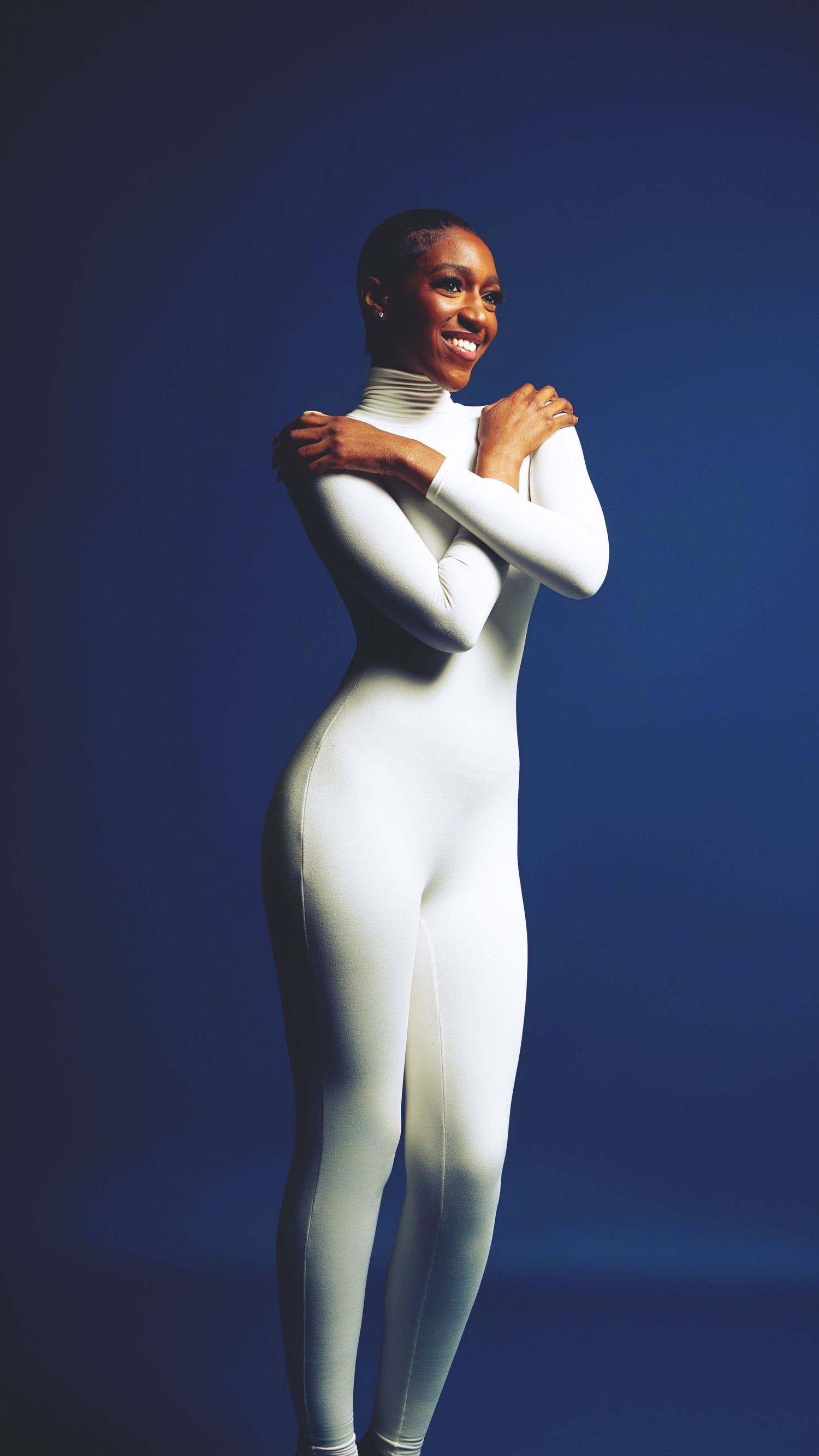 Dynamic poses in white fitted outfit against dark blue studio backdrop.