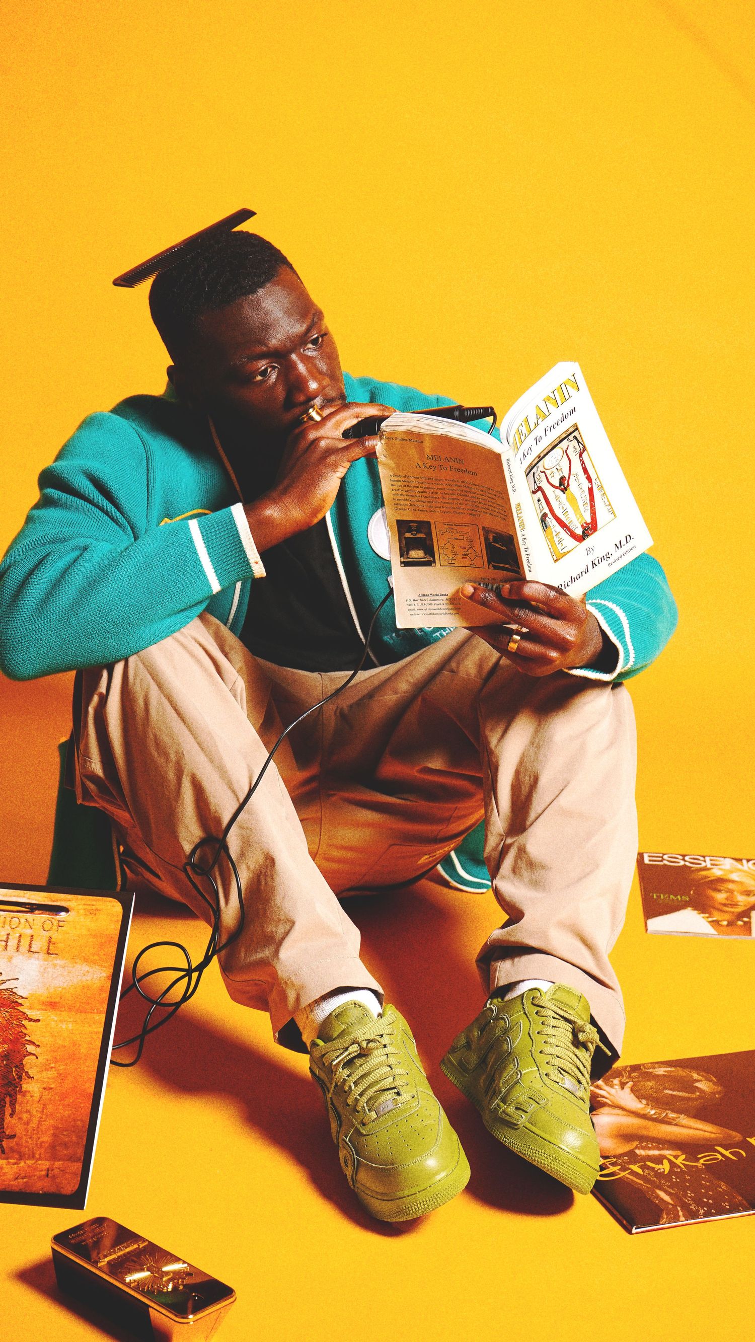 Reader in teal sweater explores books while lying on yellow background.