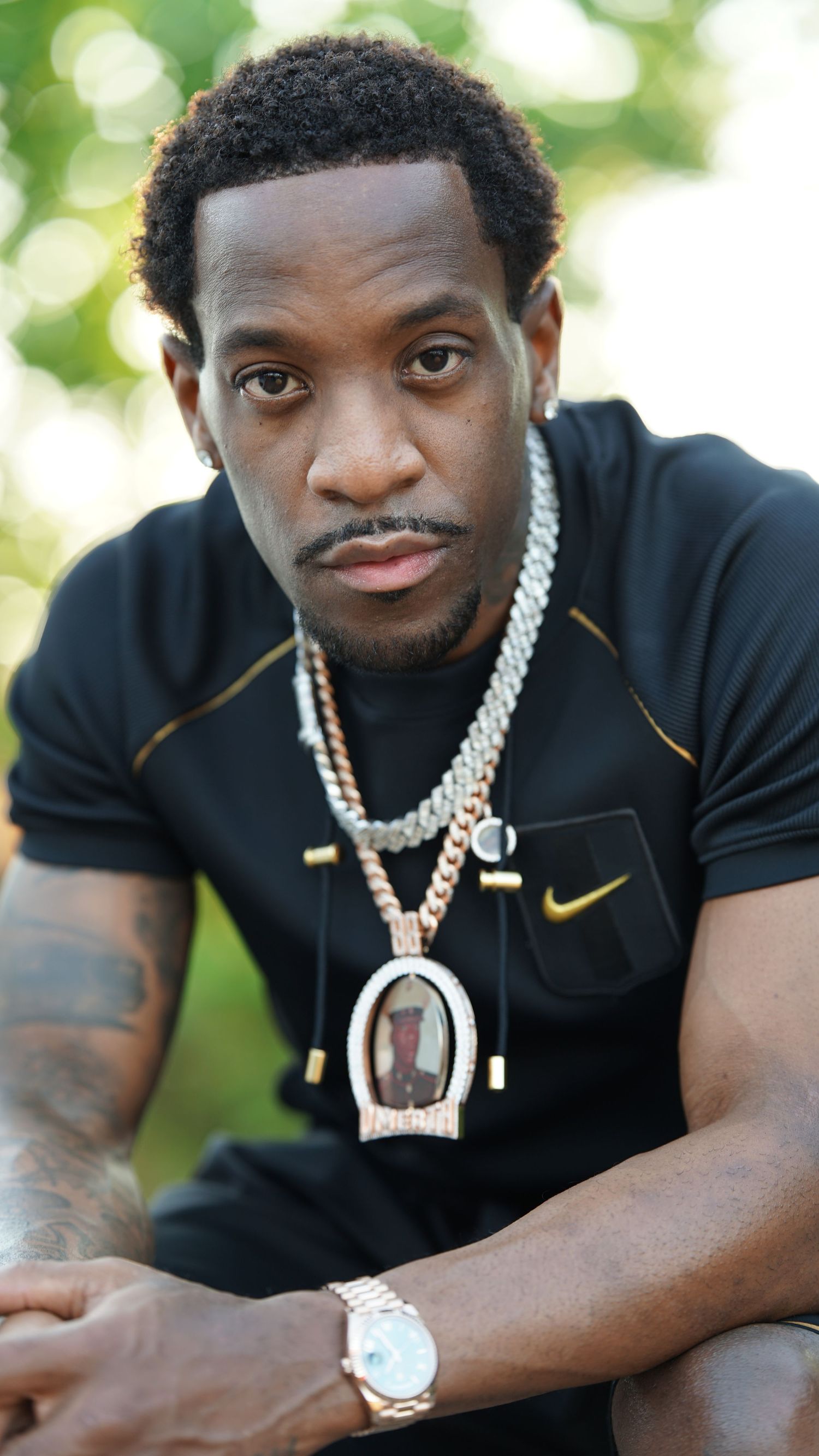 Professional athlete in black Nike shirt wearing diamond chain necklaces poses for series of closeup portraits outdoors.