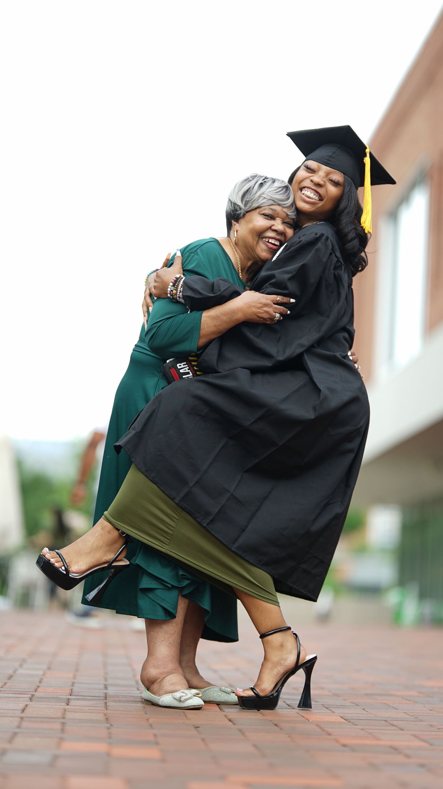Joyful graduation moment captured as supporter embraces graduate on brick walkway.