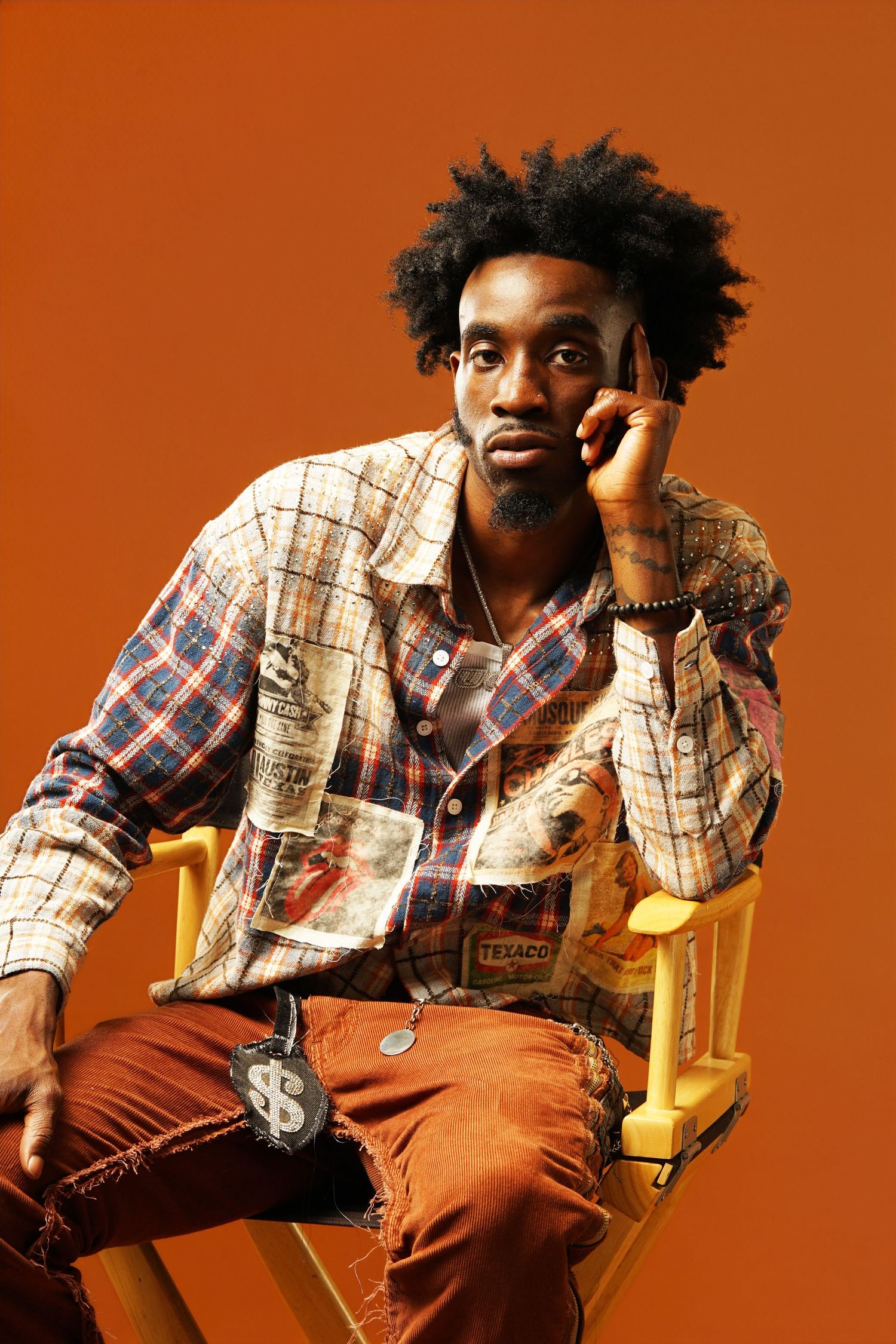 Contemplative studio portrait against orange backdrop featuring patchwork jacket and casual styling.