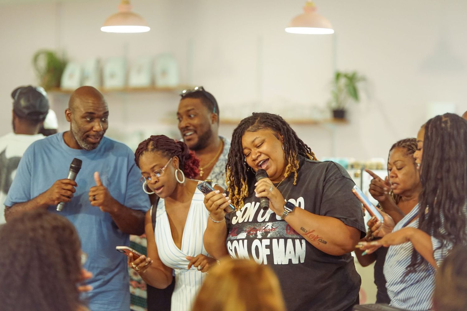Group of people singing and praising together at an indoor worship event, holding microphones and phones.