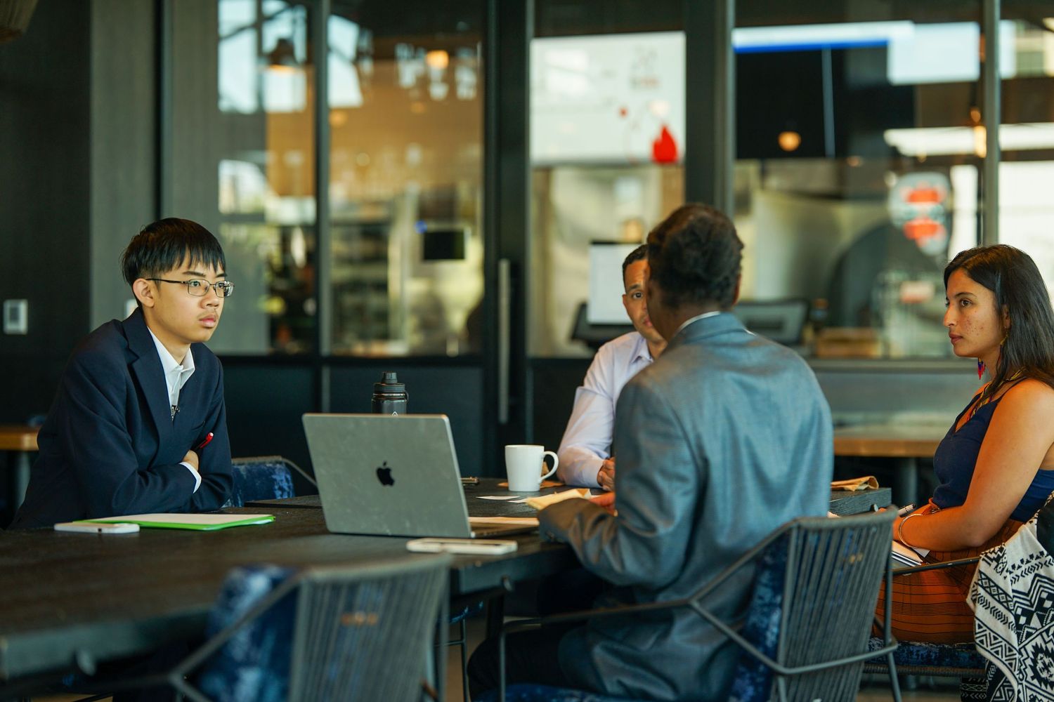 Three professionals having a business meeting at a table with an open MacBook laptop.