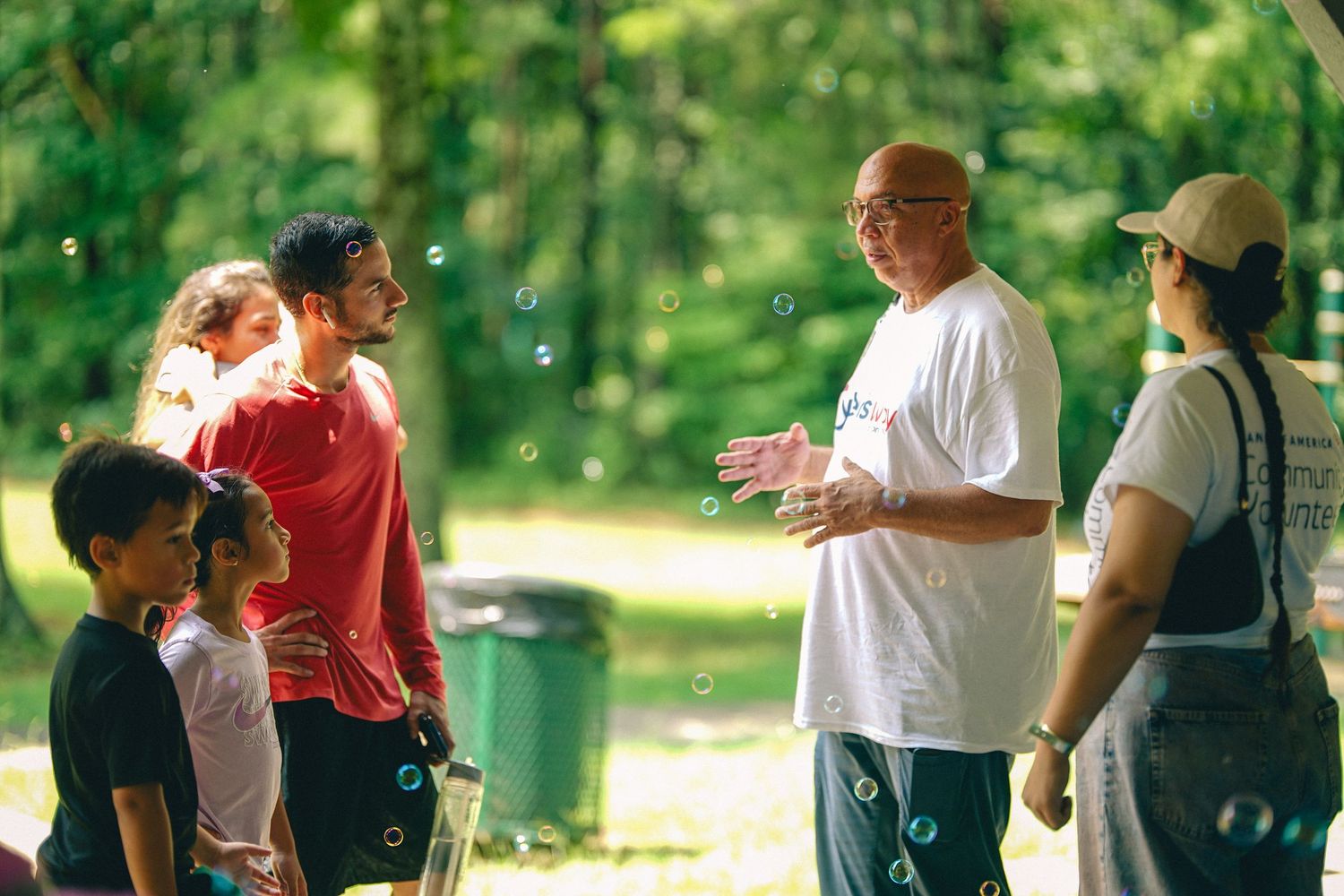 Adults and children enjoy outdoor bubbles activity in a sunny green park setting.