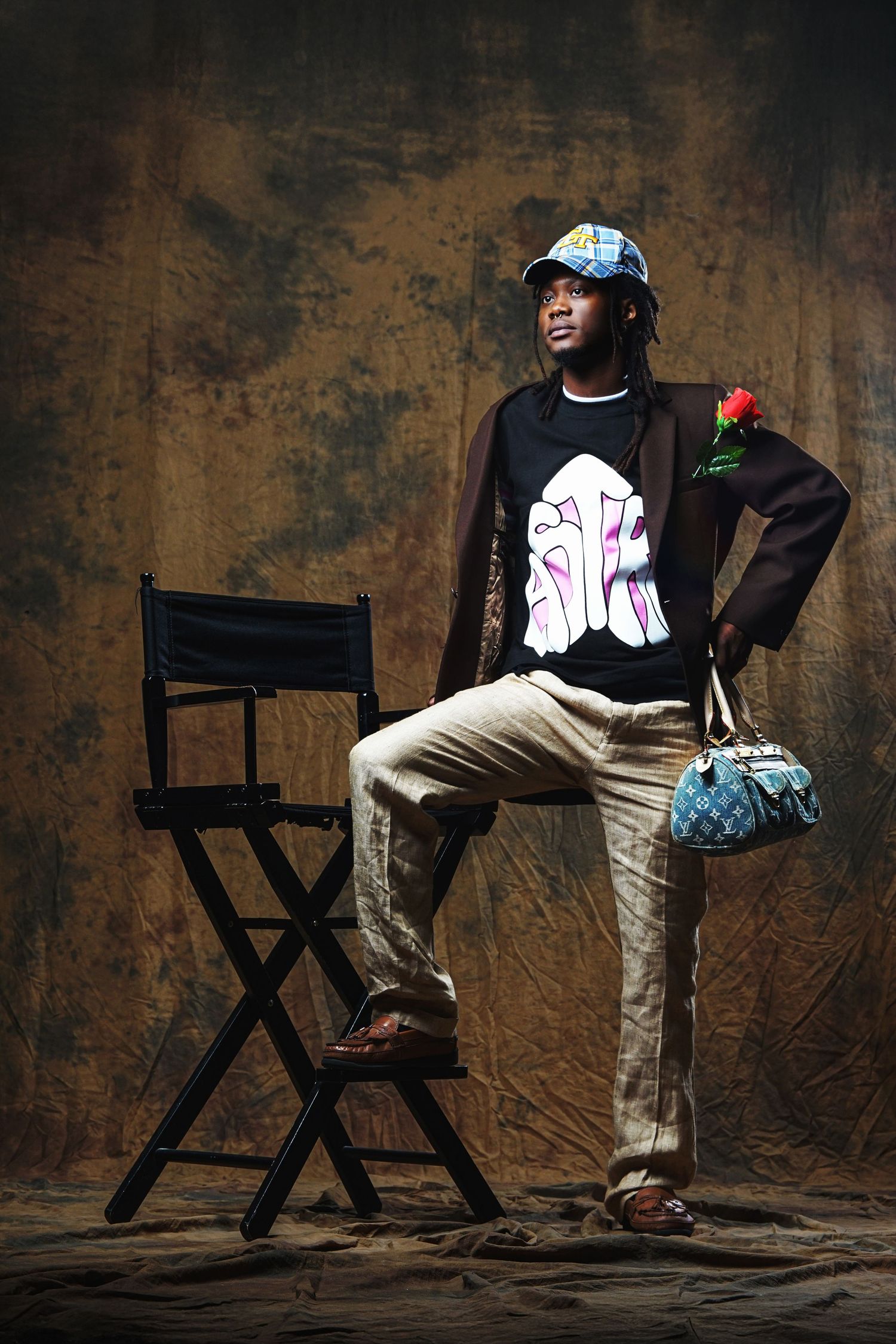 A fashion portrait featuring someone in streetwear with a blue cap and handbag against a textured brown backdrop.