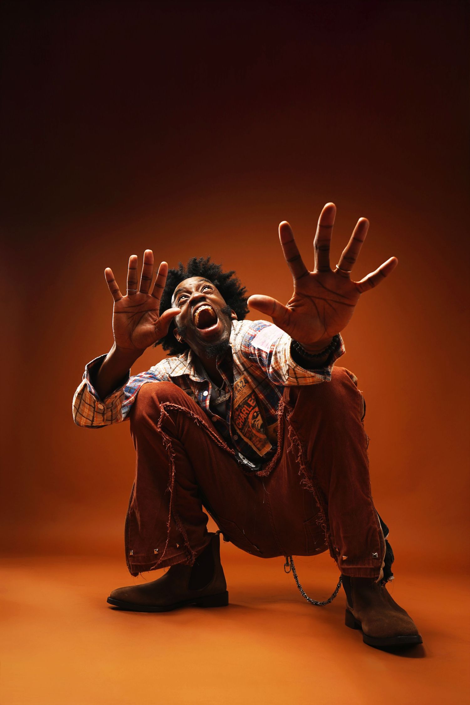 Dramatic crouching pose with outstretched hands against dark orange background.