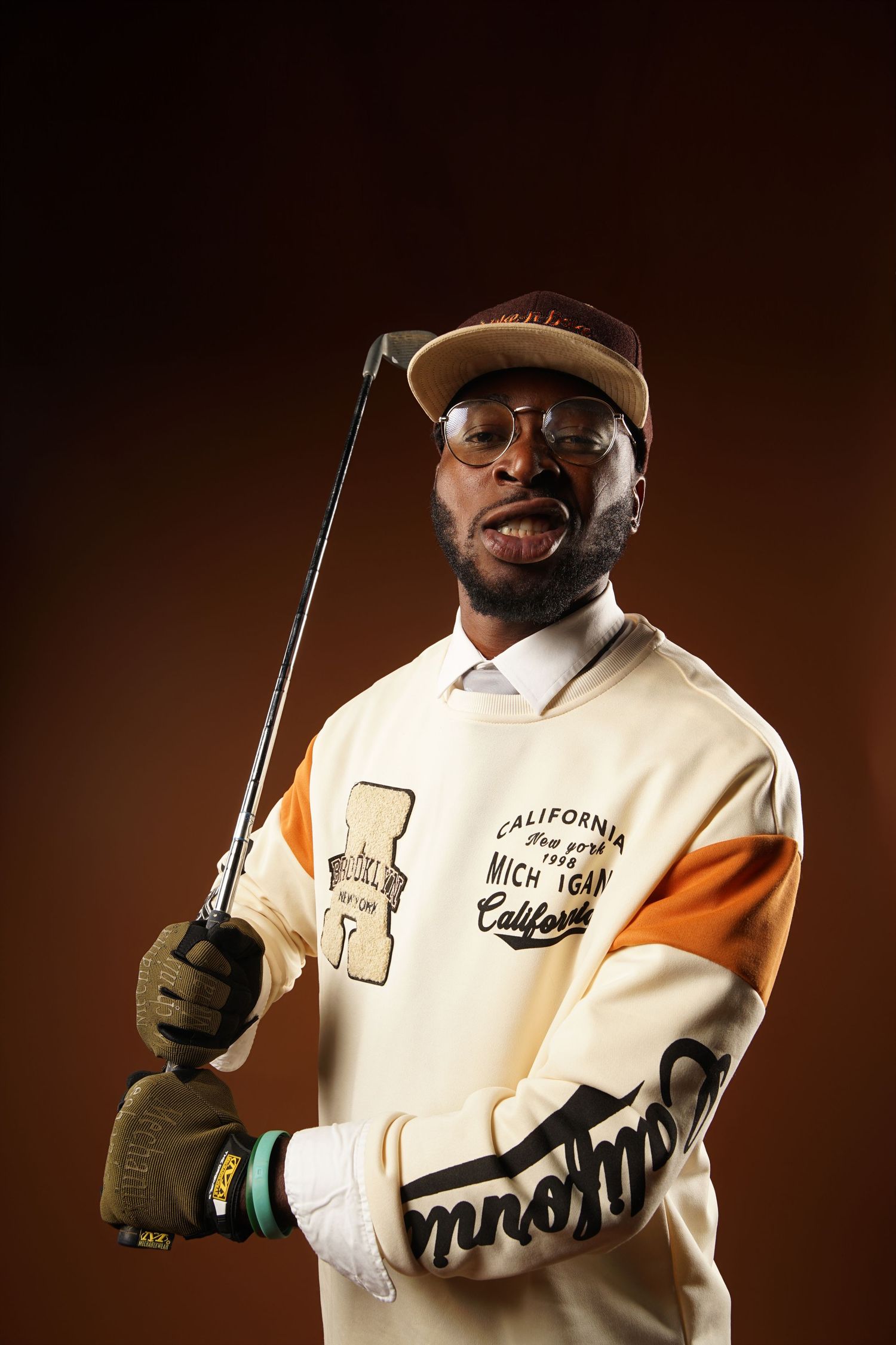 A person in a white California sweatshirt holds a conductor's baton against a dark brown background.