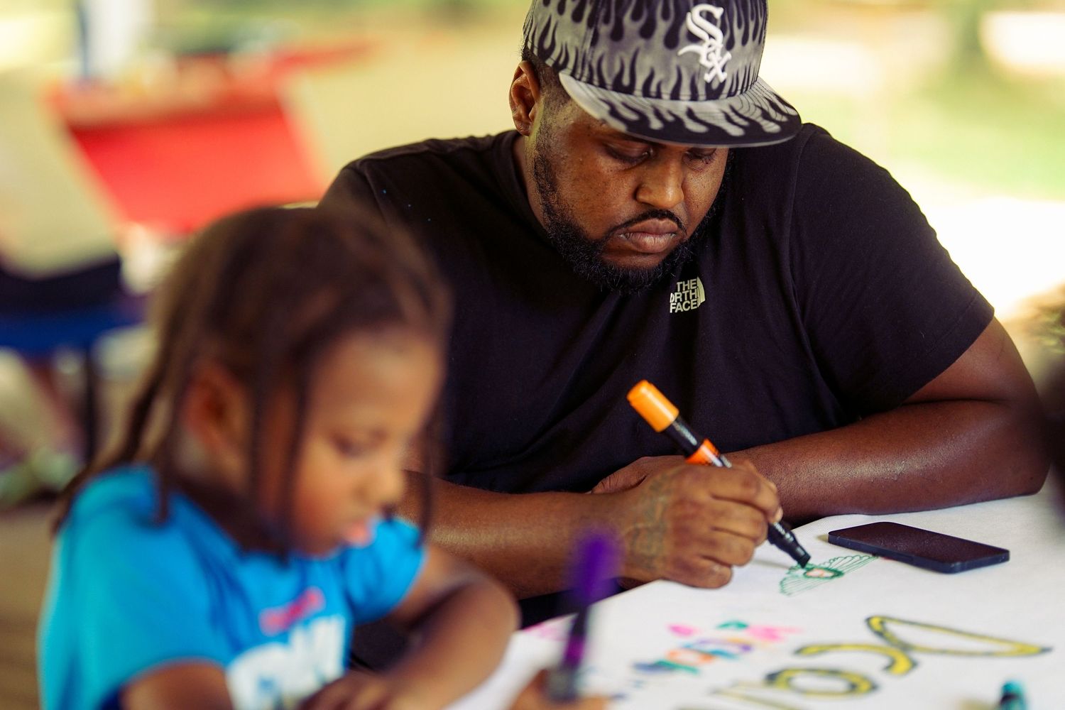 A man and young girl collaborate on a colorful drawing together at an outdoor community event.