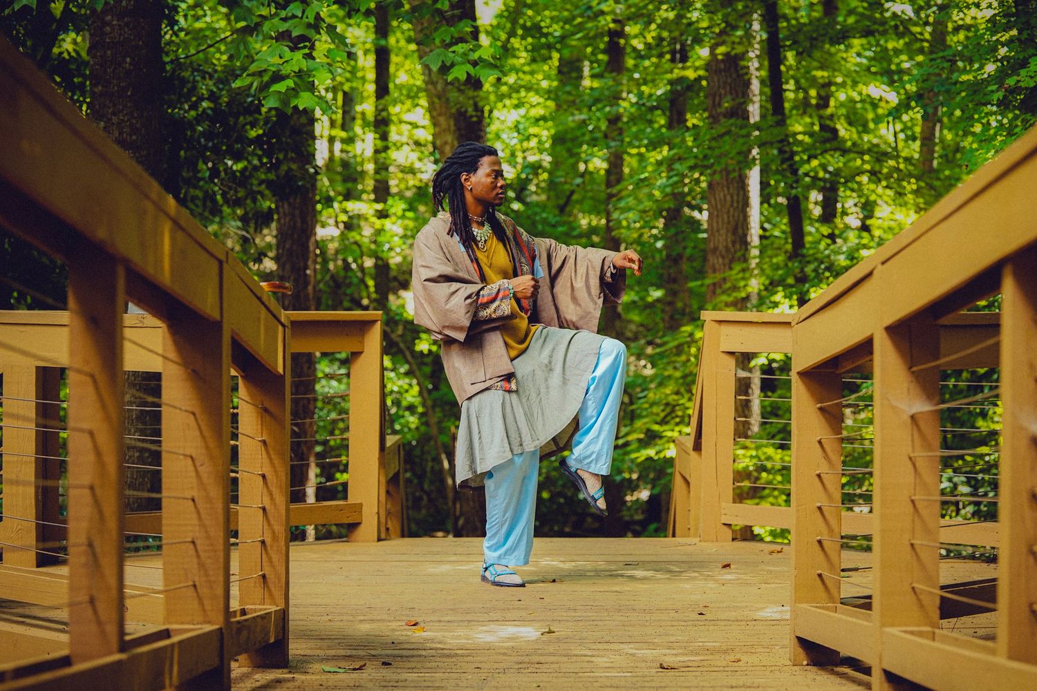 Person practicing tai chi on a wooden bridge surrounded by lush green forest trees.