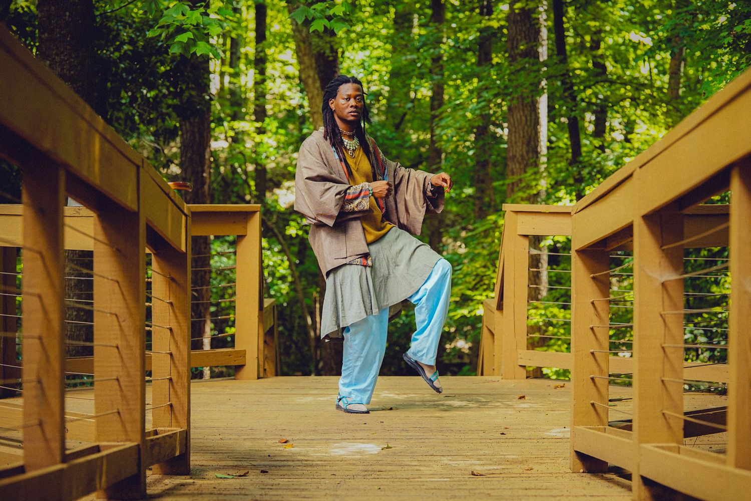 Person practicing tai chi on a wooden bridge surrounded by lush green forest trees.
