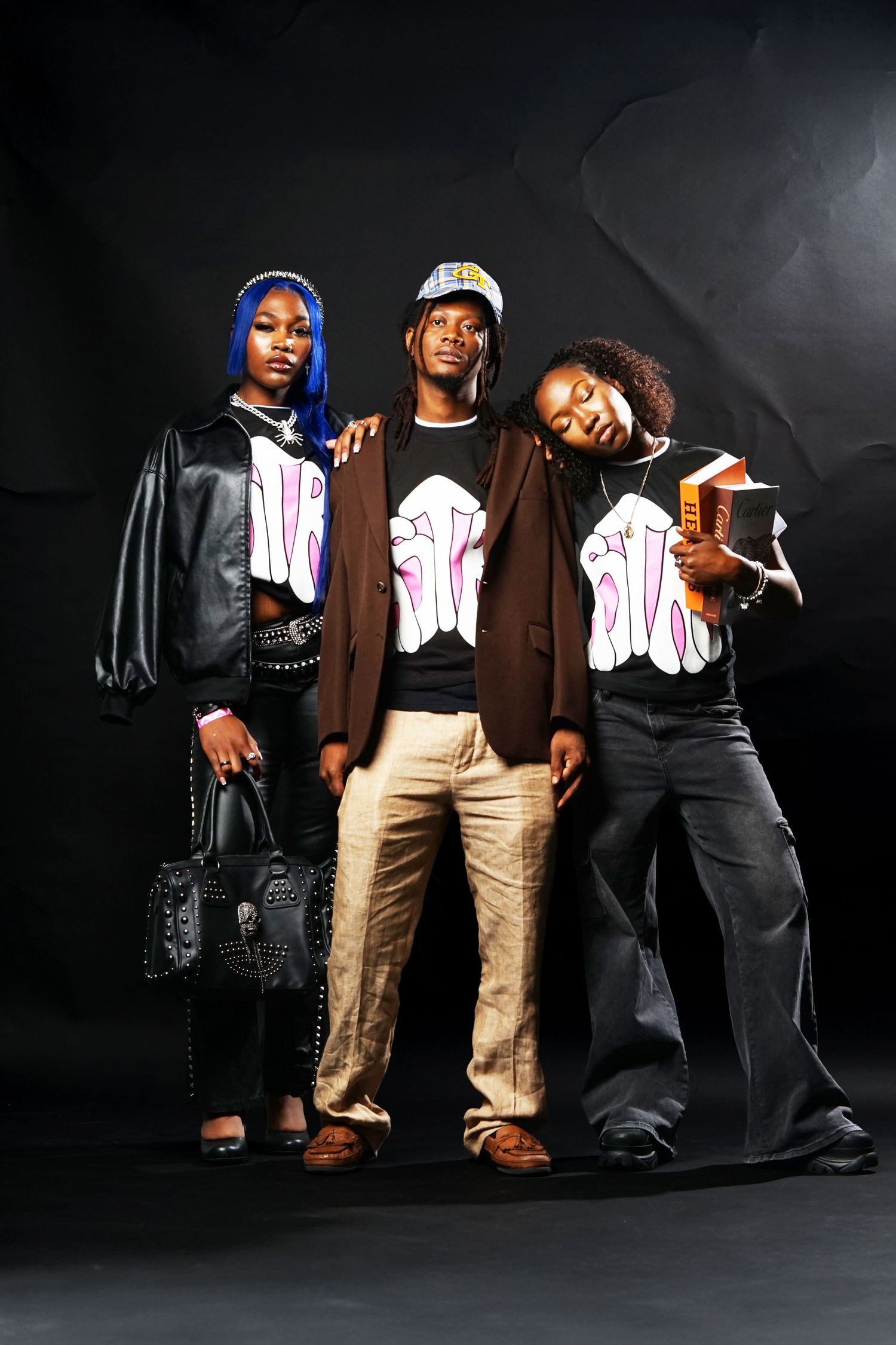 Three models posing in matching graphic t-shirts and contrasting outfits against black backdrop.