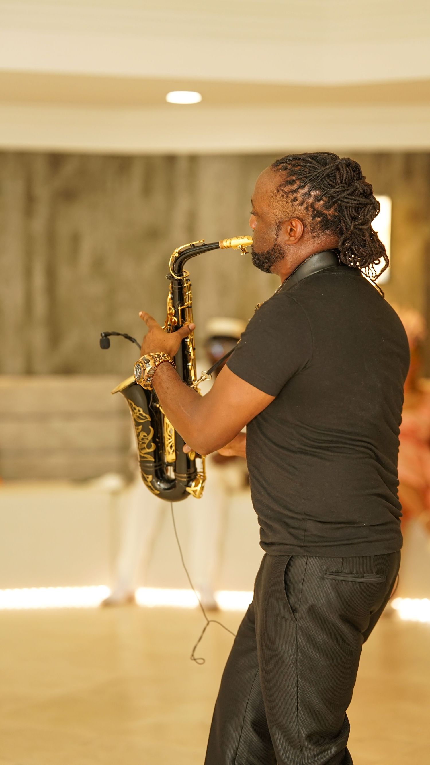 Musician plays saxophone in a dimly lit venue wearing black attire.
