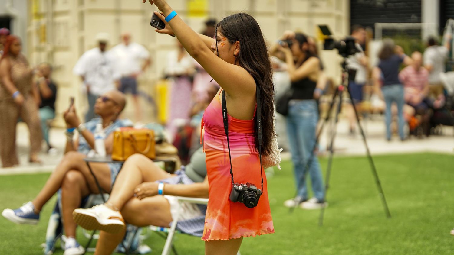 People enjoying an outdoor performance on a sunny day with colorful clothing and cameras.