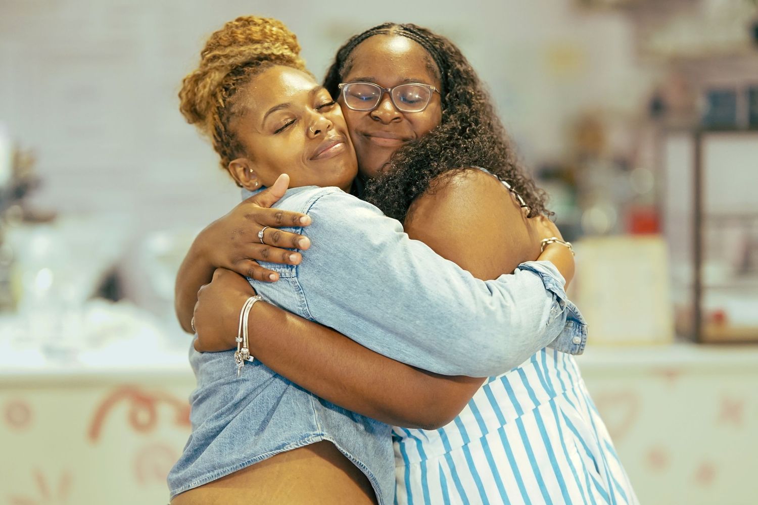 Two women share a warm, joyful hug while smiling at an indoor gathering event.