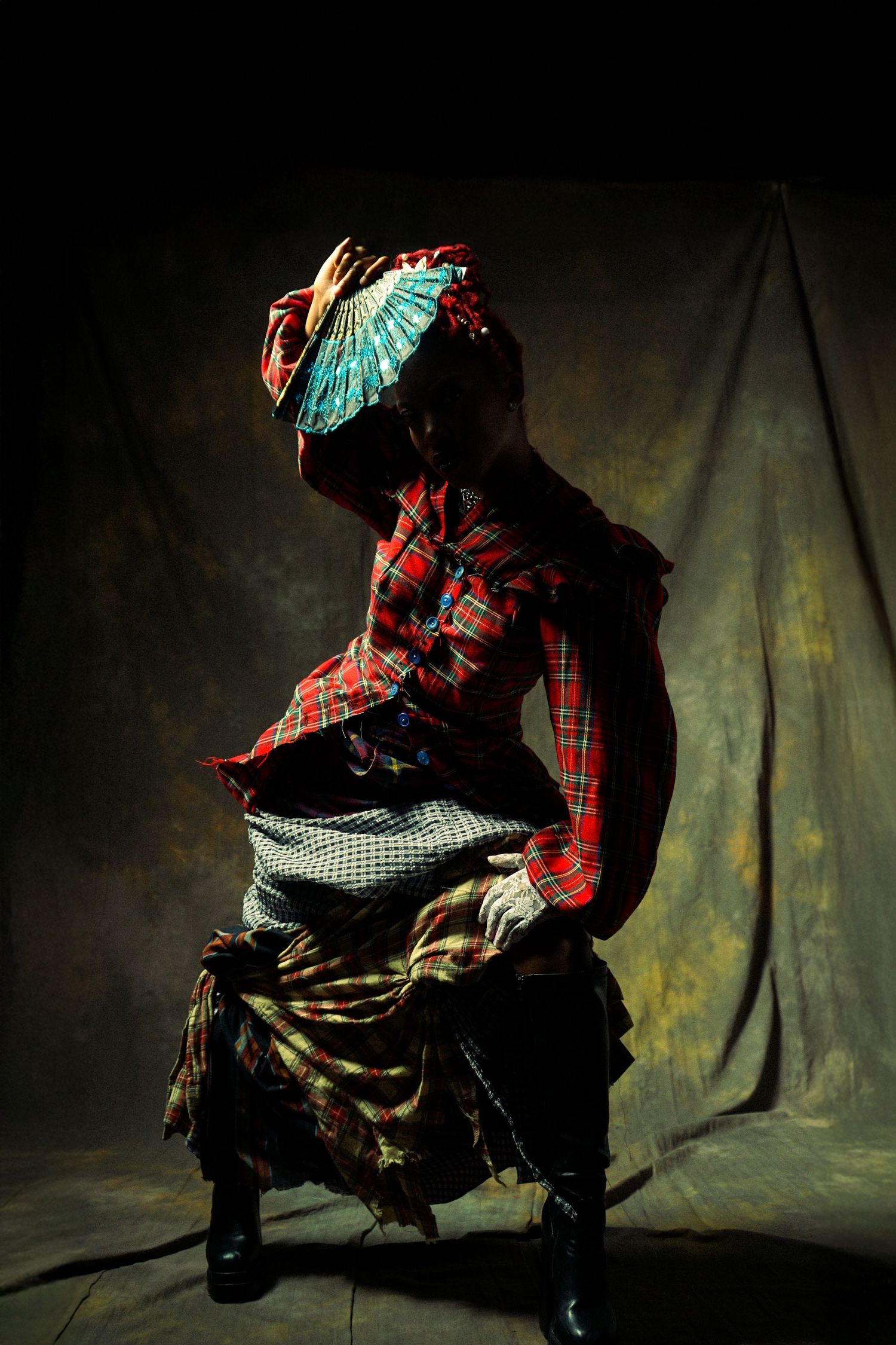 A figure in red plaid and dark clothing performs dynamic dance moves in a dramatic low-light setting.