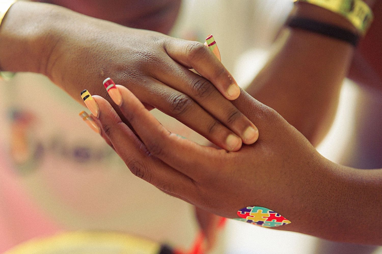Close-up of two dark-skinned hands with colorful painted nails gently touching outdoors.