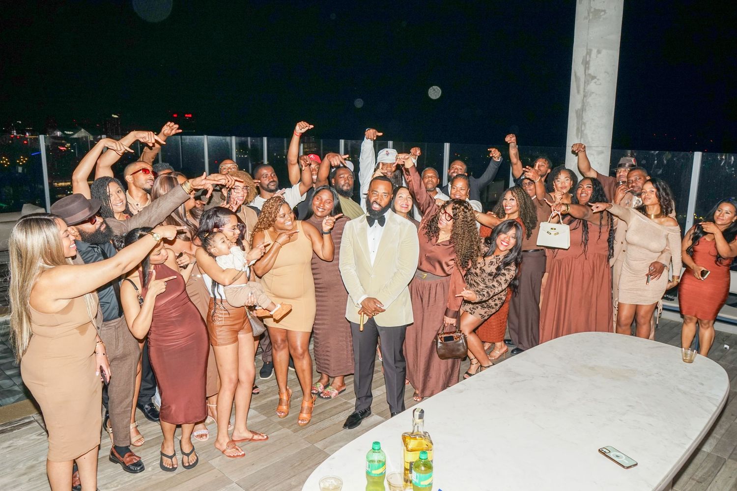 Large group of elegantly dressed guests celebrating at an outdoor nighttime party event on a rooftop or deck.
